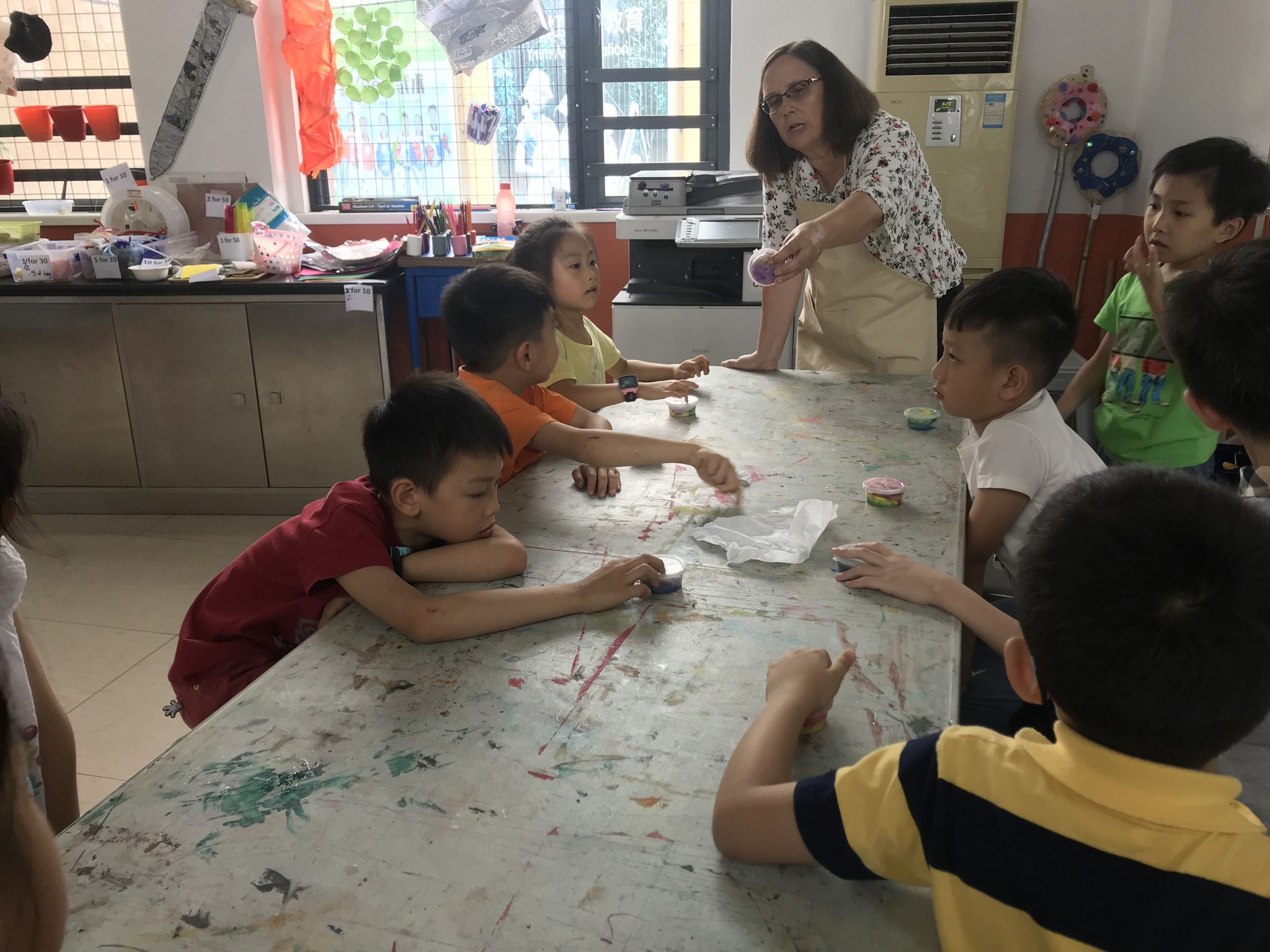 Twila Busby demonstrating a craft material to a group of children gathered around a table