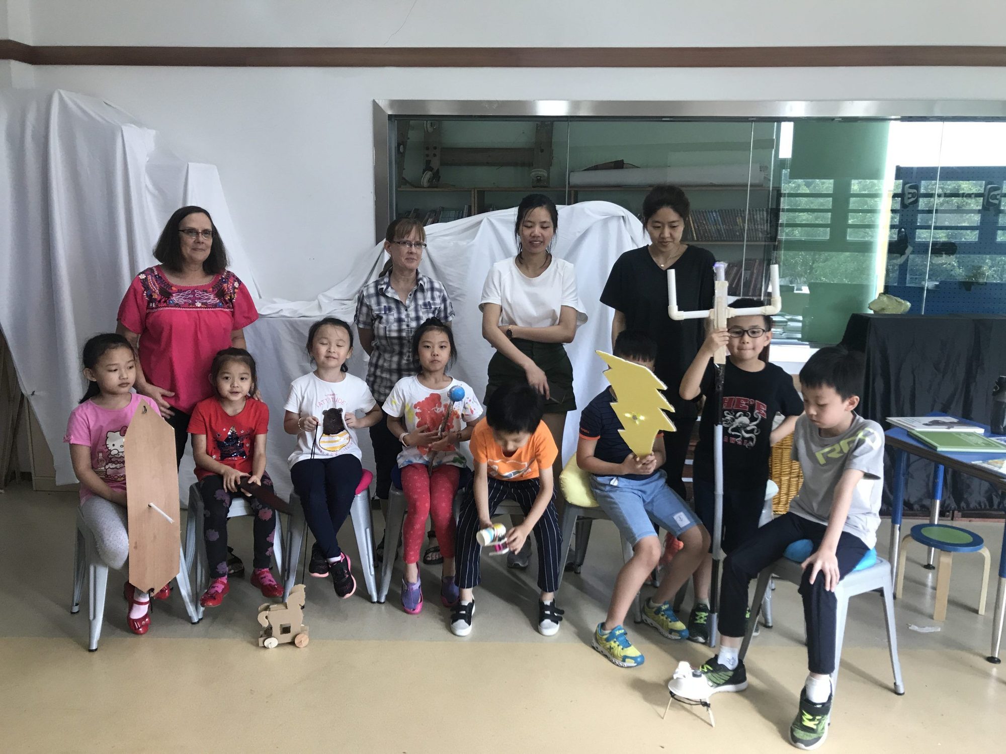 Twila Busby standing with a group of seated students holding cardboard and craft inventions