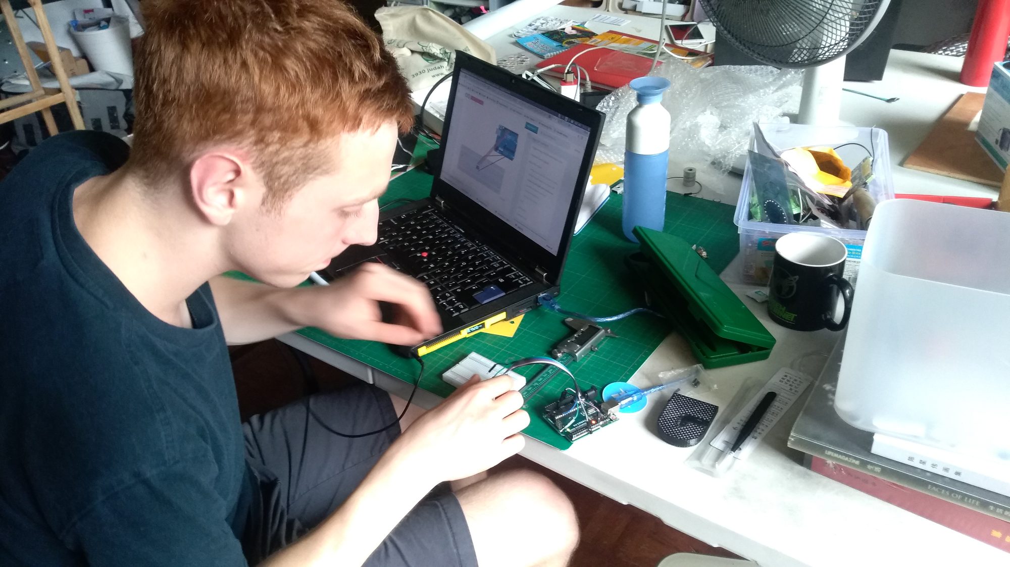 Young man soldering an Arduino project at a cluttered workbench