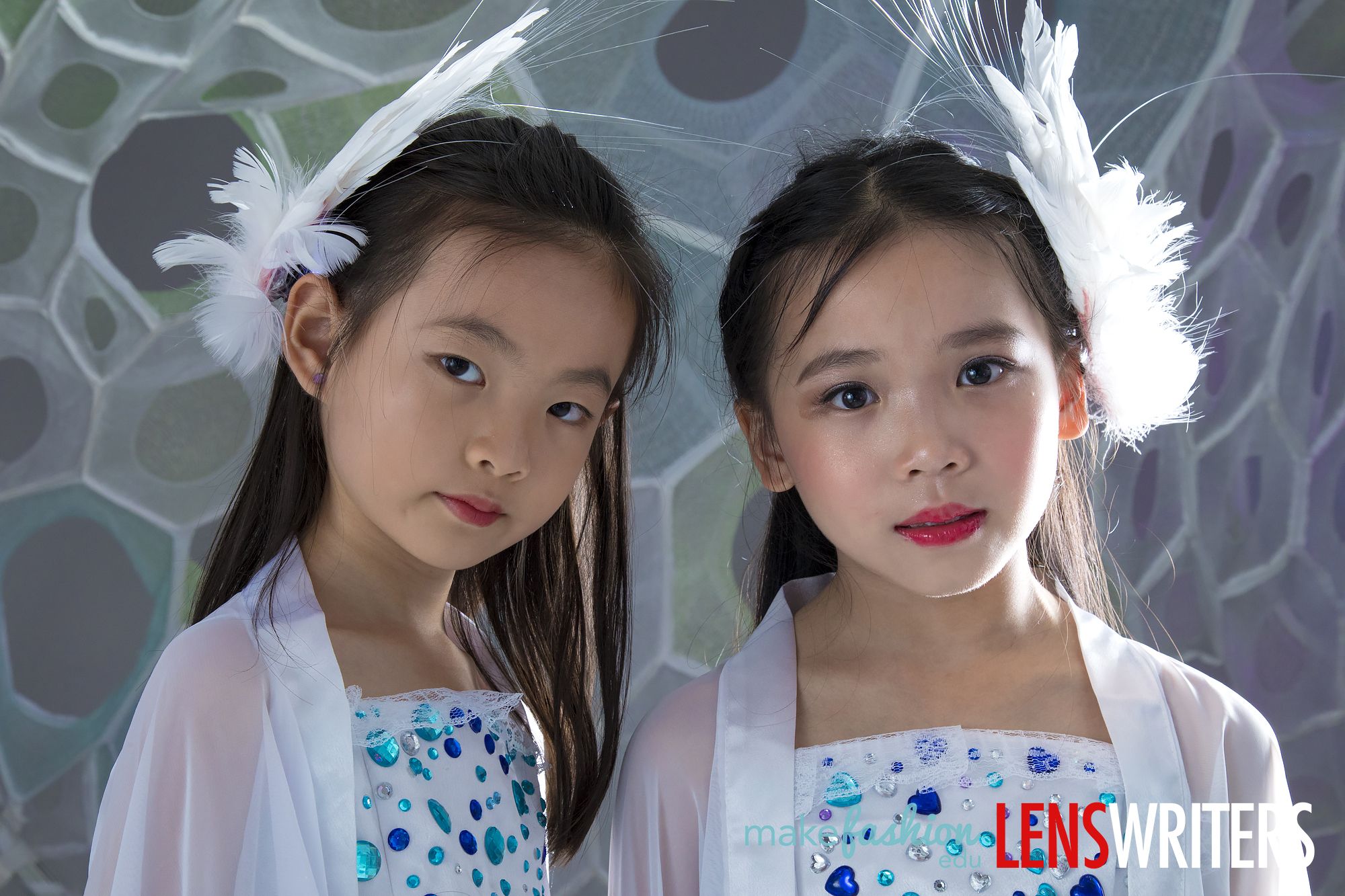 Two students in matching white LED dresses with feather headpieces