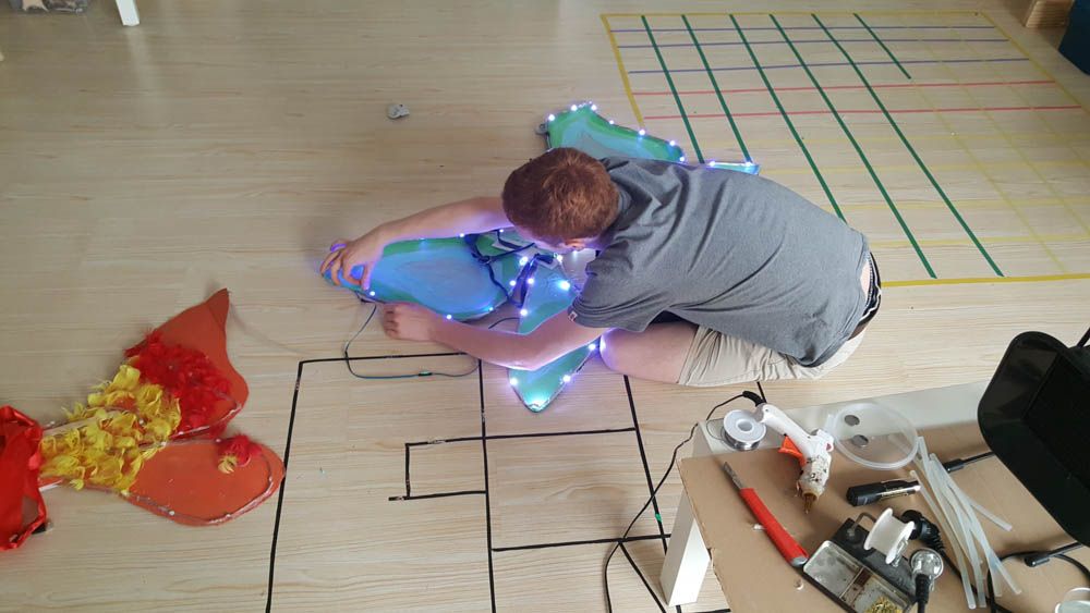 Oliver Child kneeling on the floor attaching LED lights to a fabric costume piece