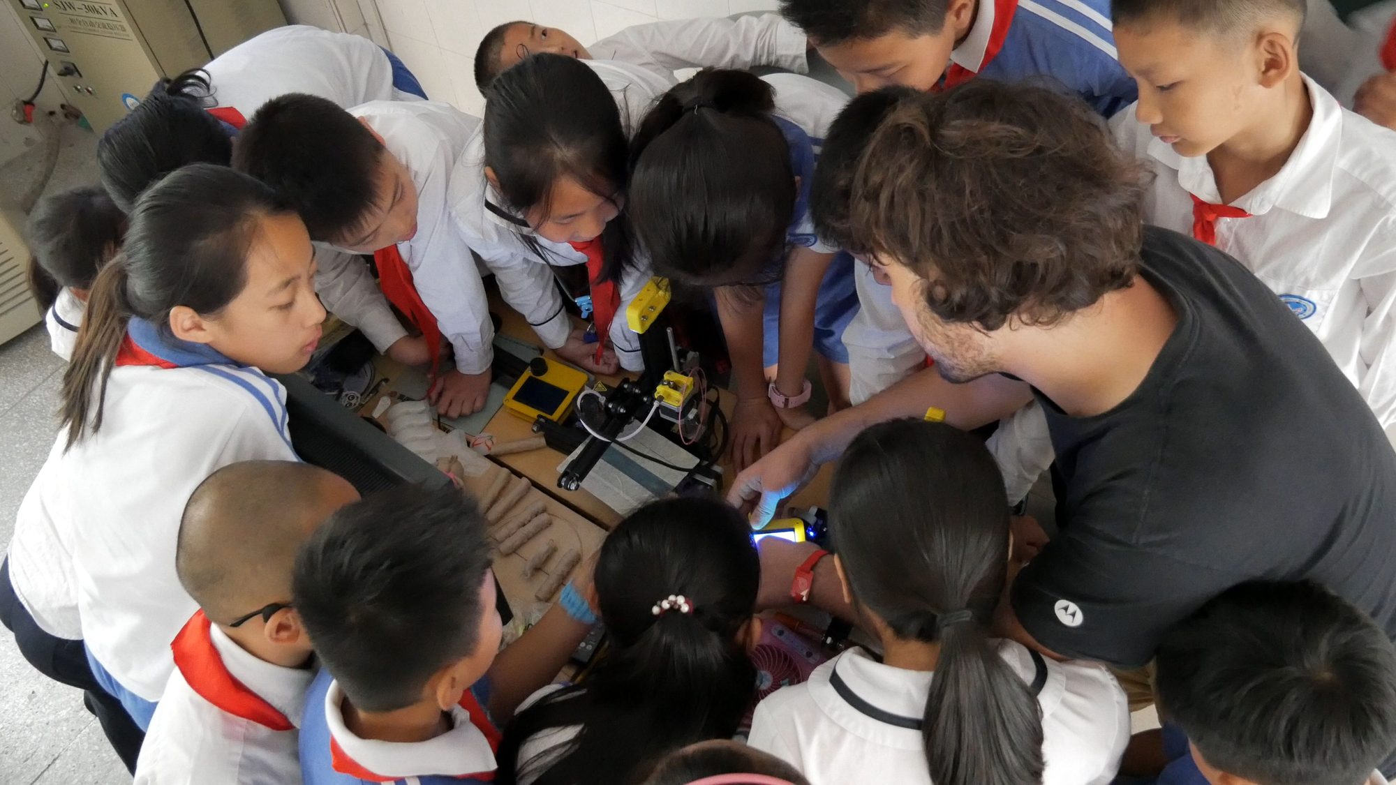 Students and a teacher crowded around a desktop 3D printer