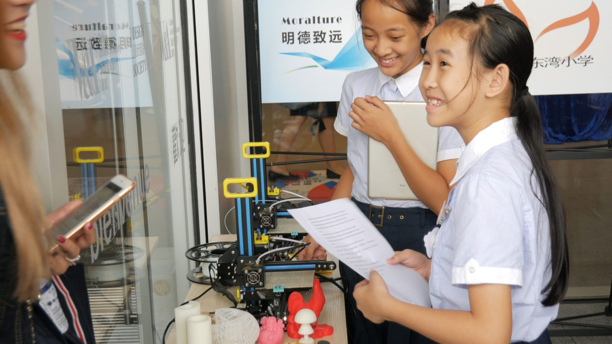 Two students smiling beside a 3D printer and printed models