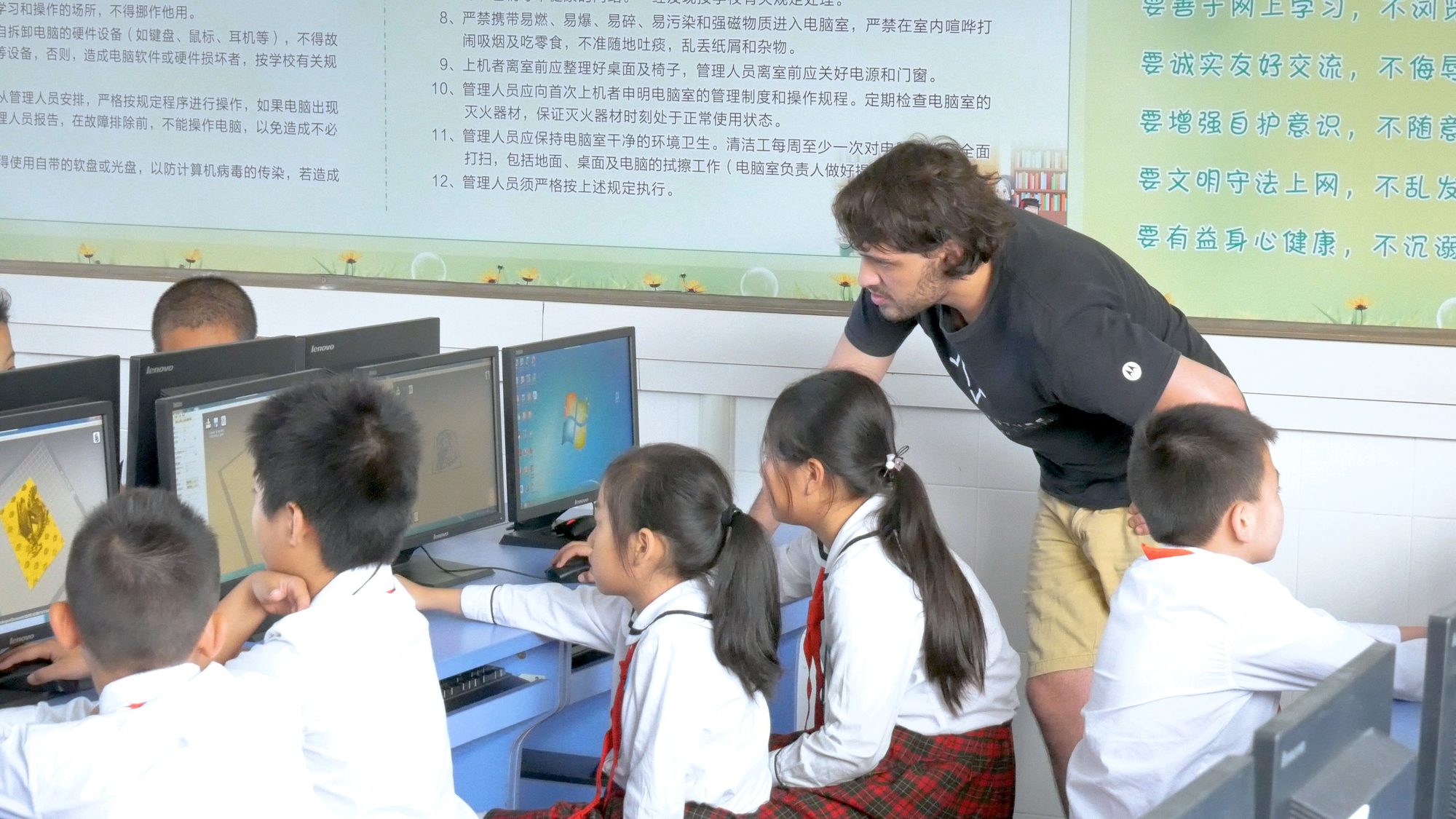 Teacher leaning over students at computers running 3D design software