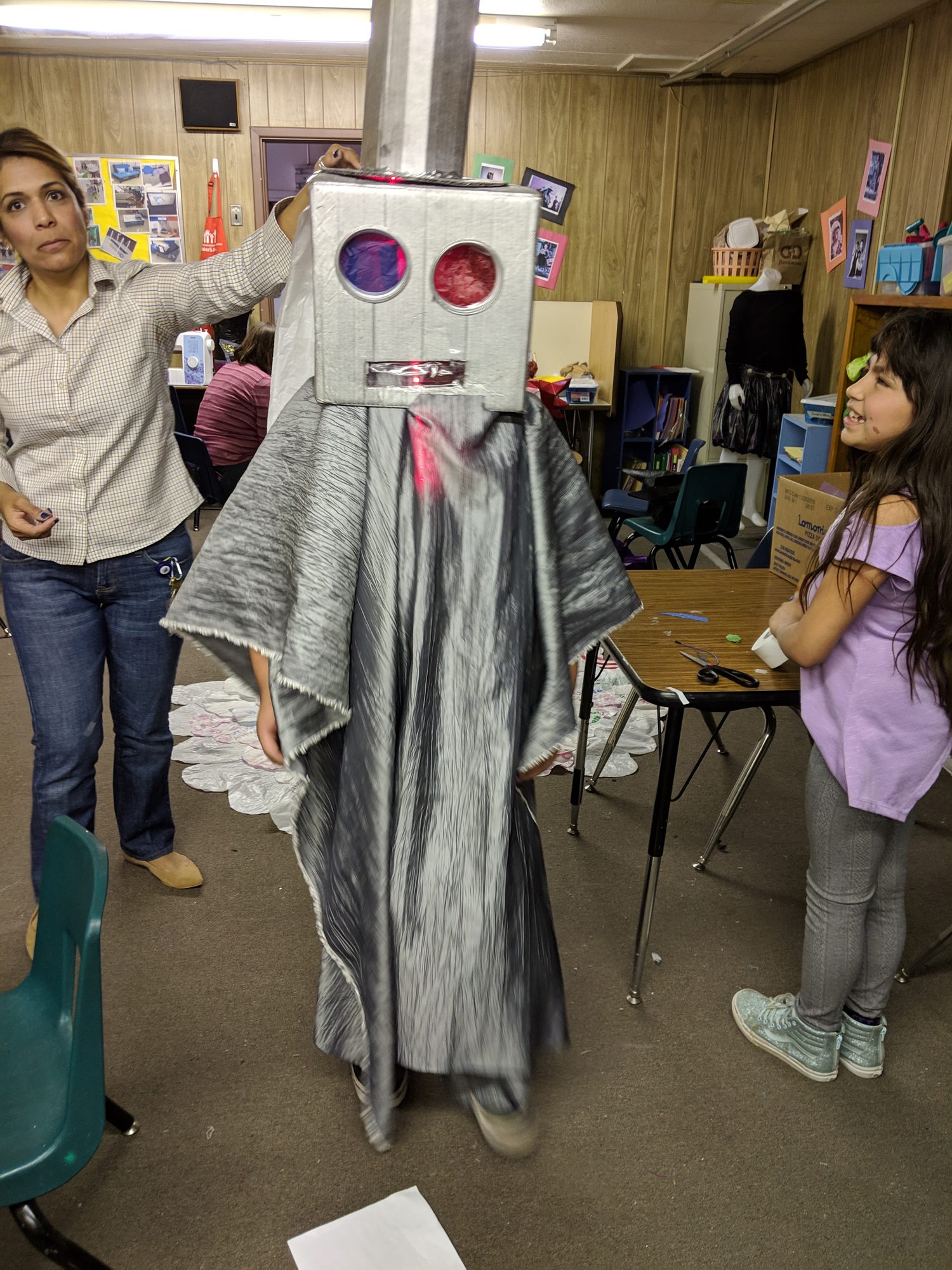 Illuminated robot costume held up in a classroom with a student watching