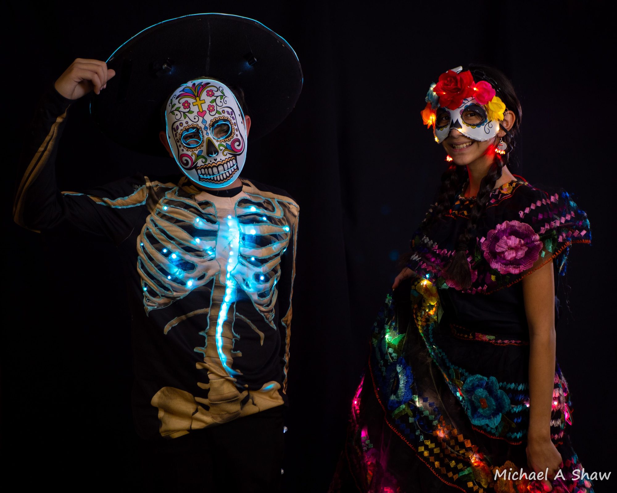 Two students in illuminated sugar skull masks and LED costumes