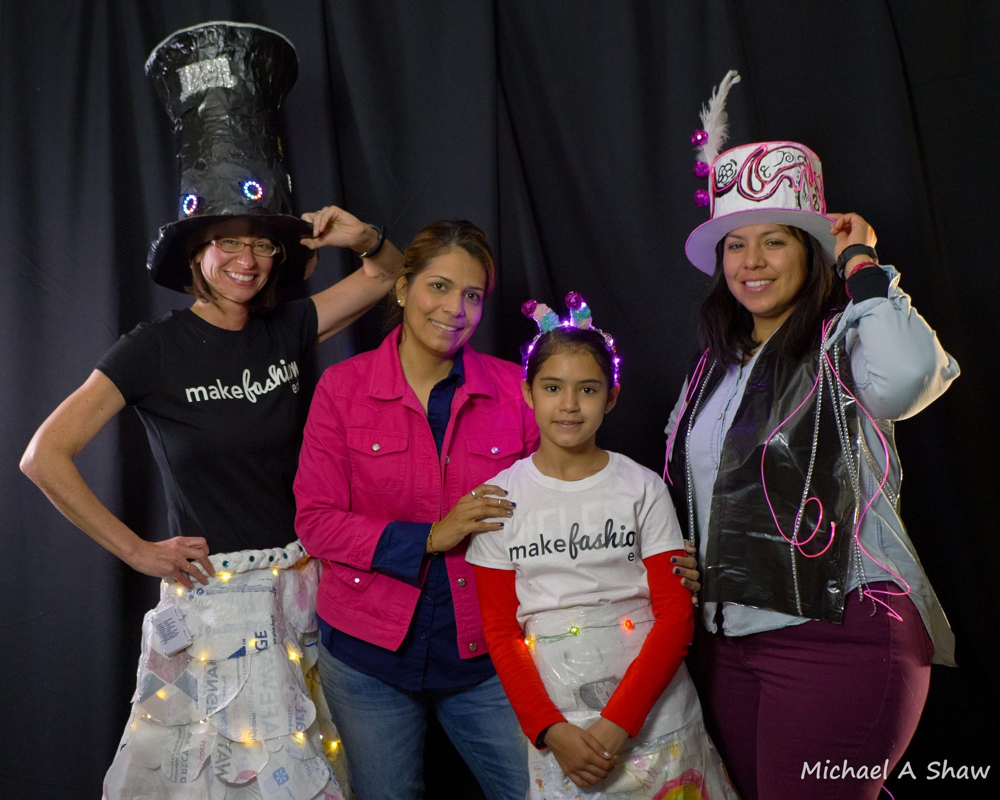 Two adults and a student model glowing LED top hats and headbands