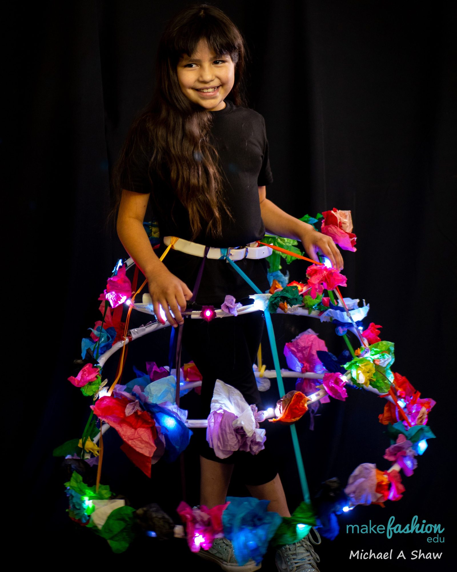 A student wearing an illuminated hoop skirt with paper flowers