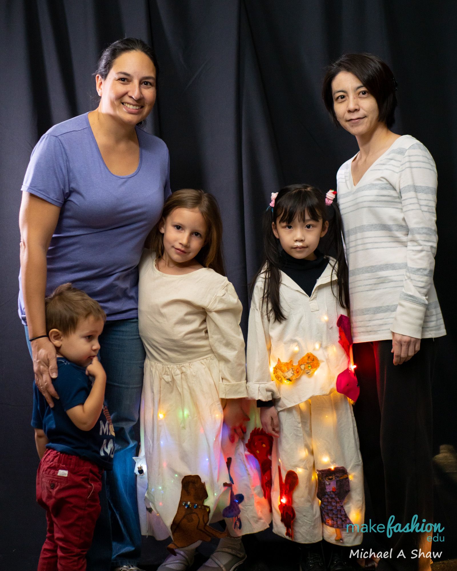 Two women with two students in glowing cream costumes and a toddler boy