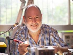 Paul soldering a circuit board, smiling at the camera