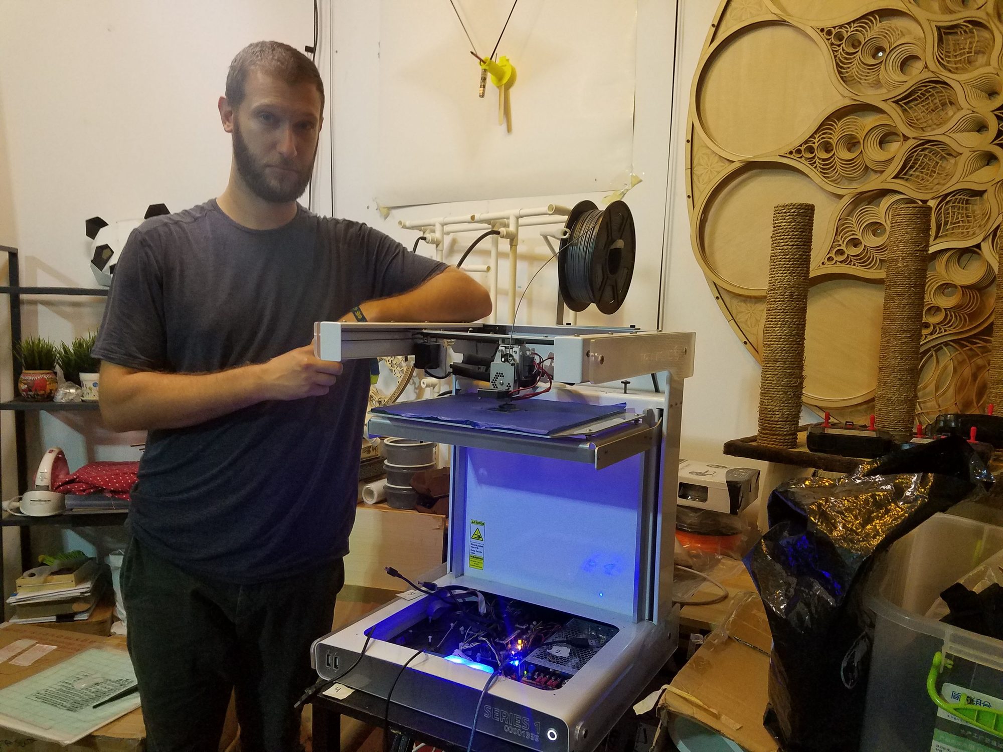 Man standing beside a large open-frame 3D printer