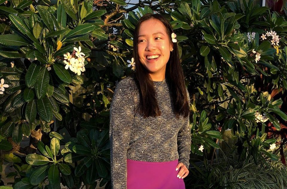 Lauren smiles in front of a flowering frangipani tree
