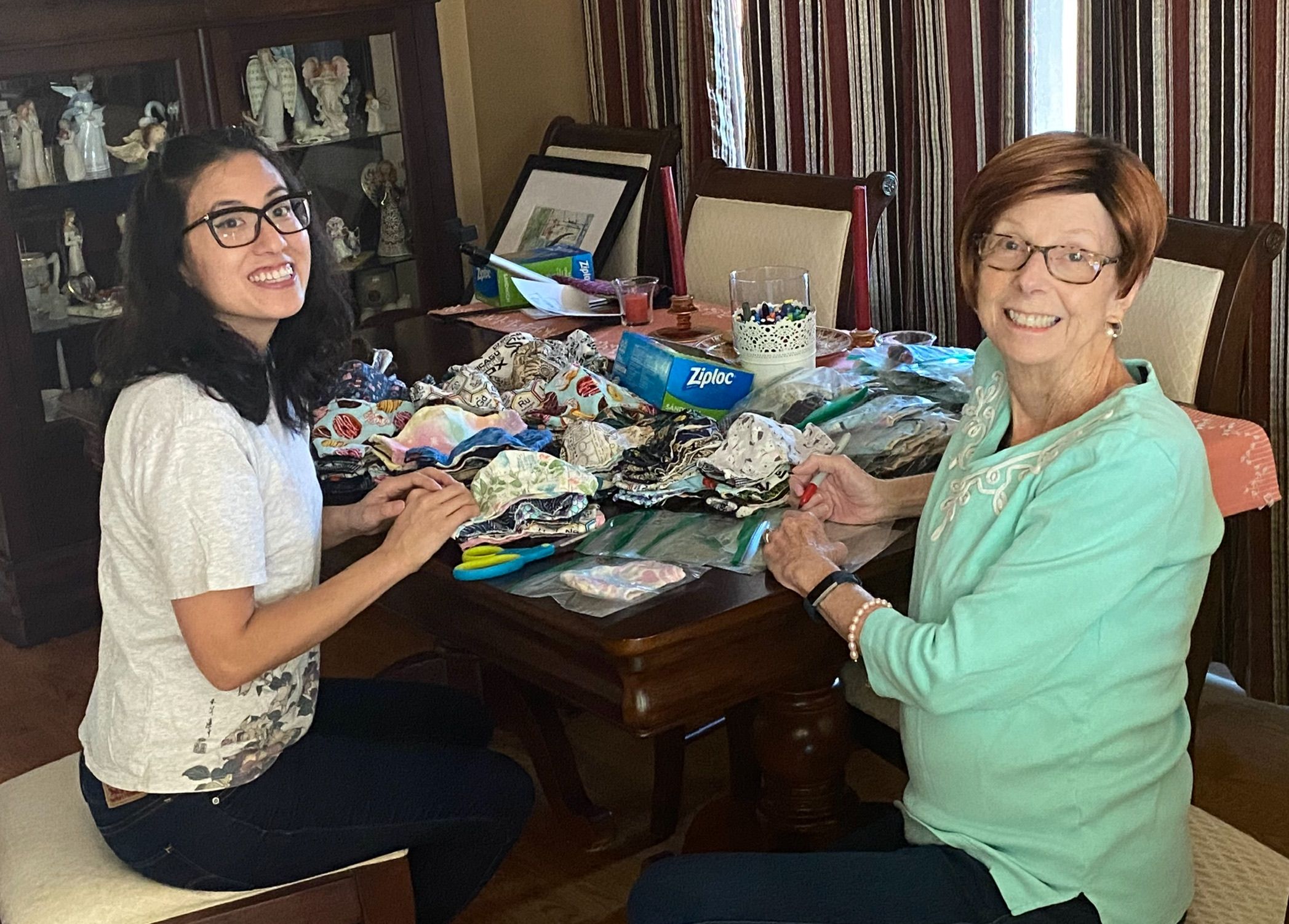 Two women sitting at a table sorting handmade cloth face masks