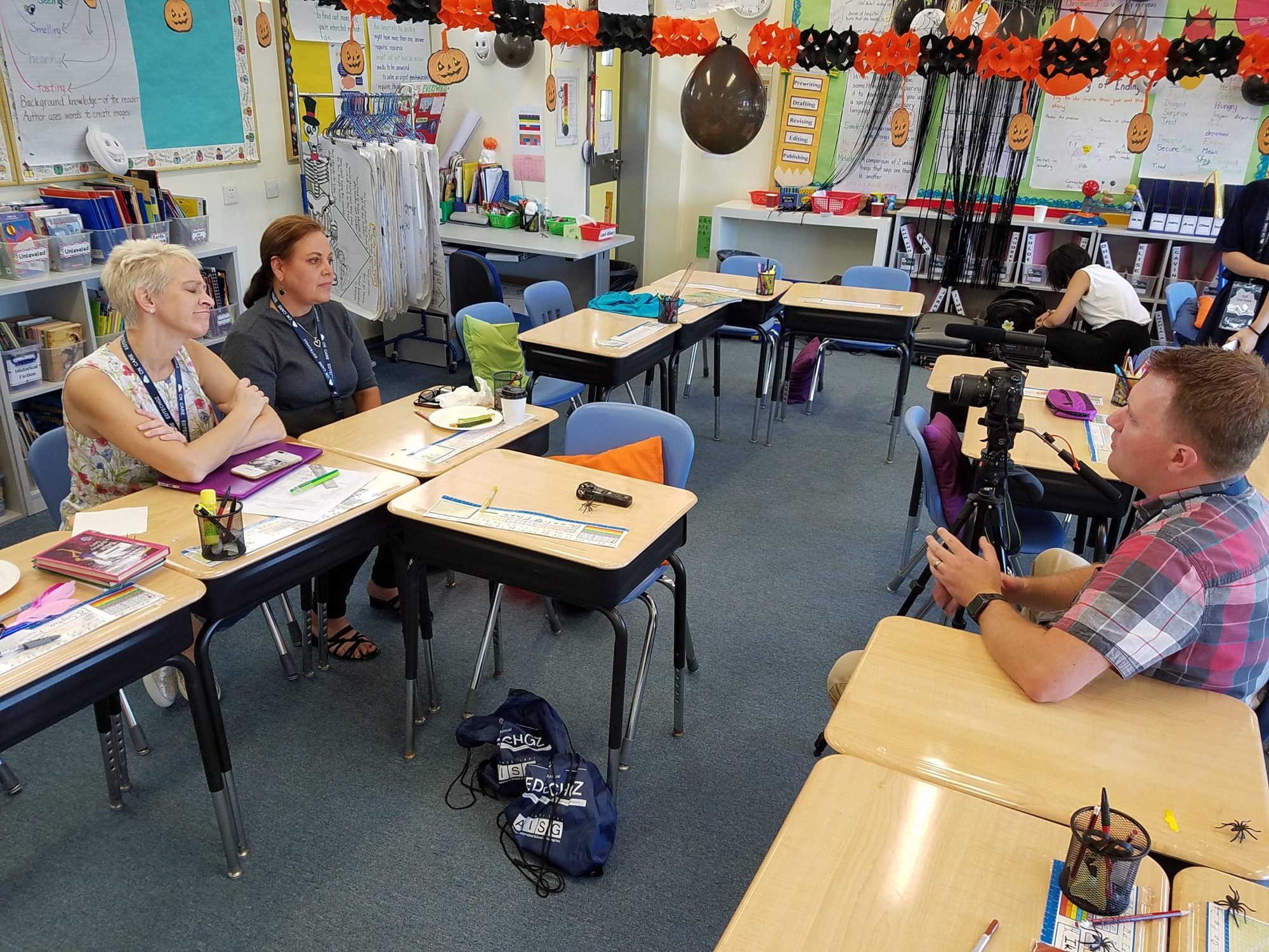 Two teachers interviewed on camera in a Halloween-decorated classroom
