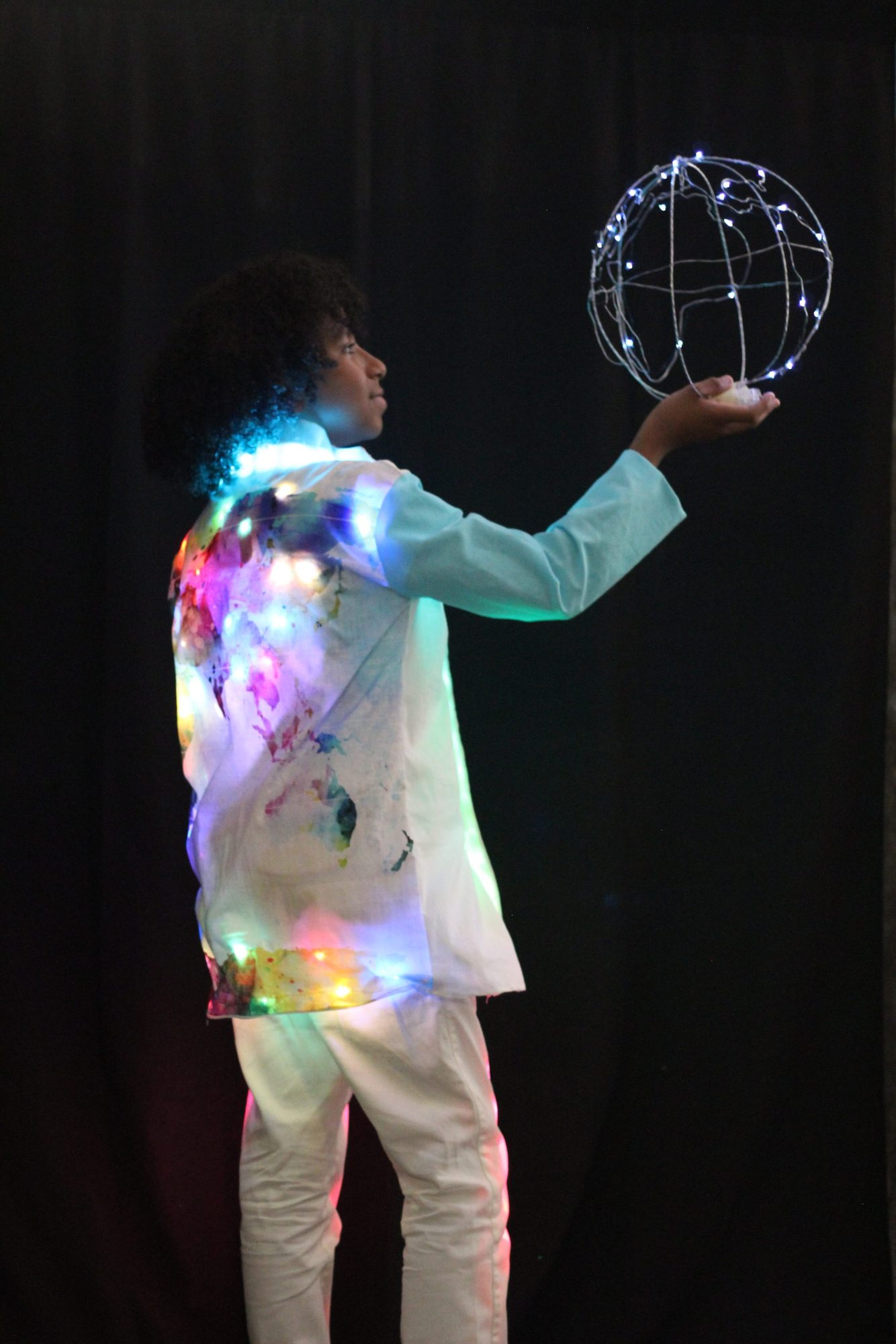 Student holding a glowing wire globe sculpture in an LED-covered shirt