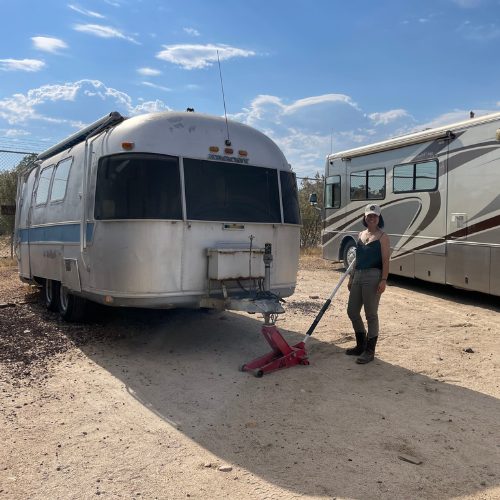Mobile Makerspace chapter 6: a volunteer posing with a floor jack beside the parked Airstream