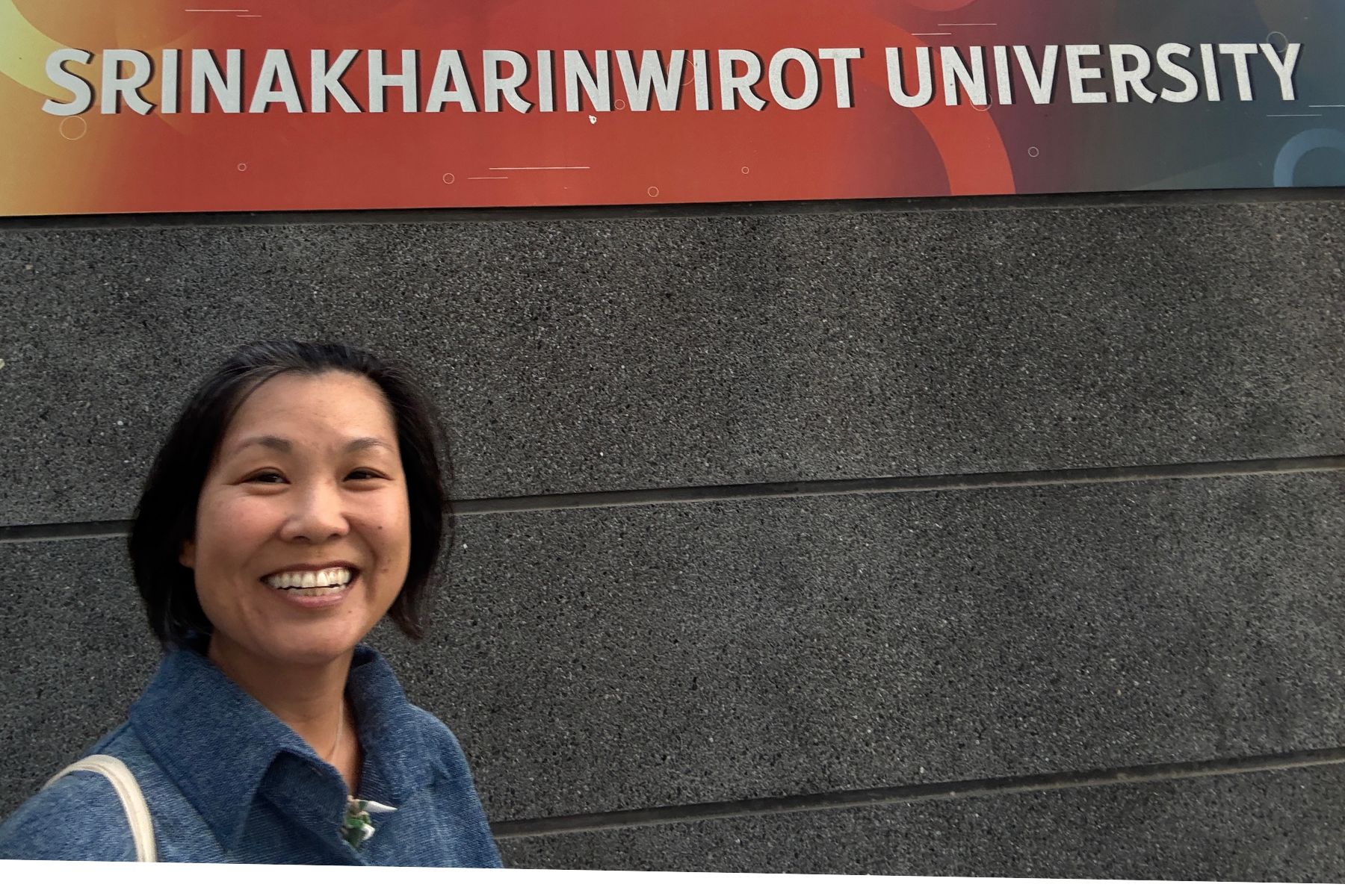 Woman smiling beside the Srinakharinwirot University sign