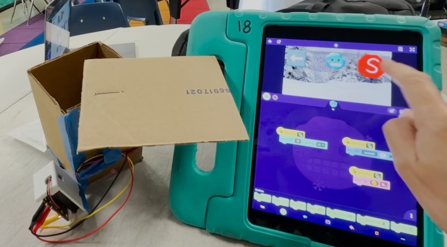 Cardboard snow-release box beside a tablet running OctoStudio
