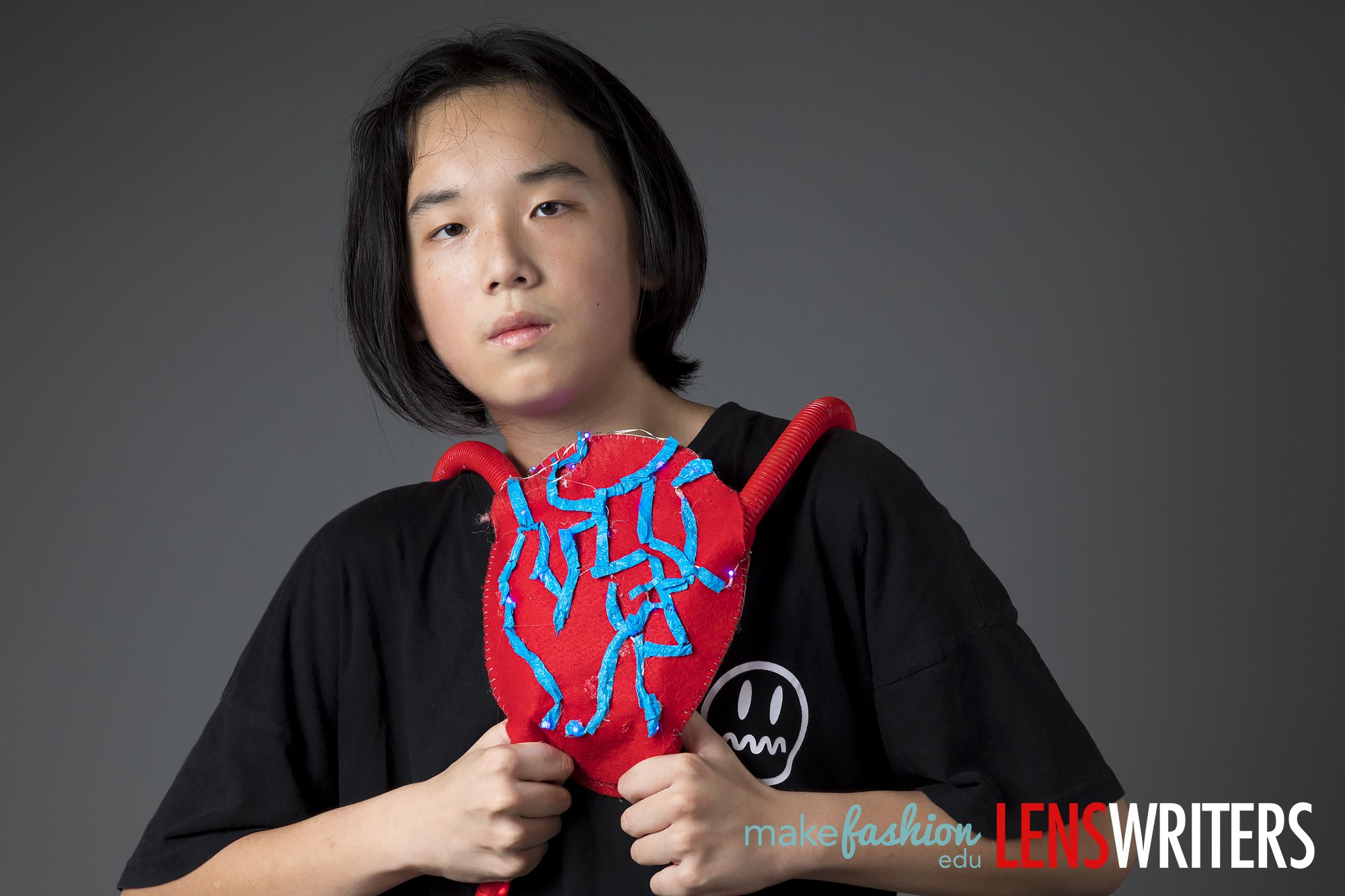 Student model holding red heart-shaped wearable with blue LED thread pattern