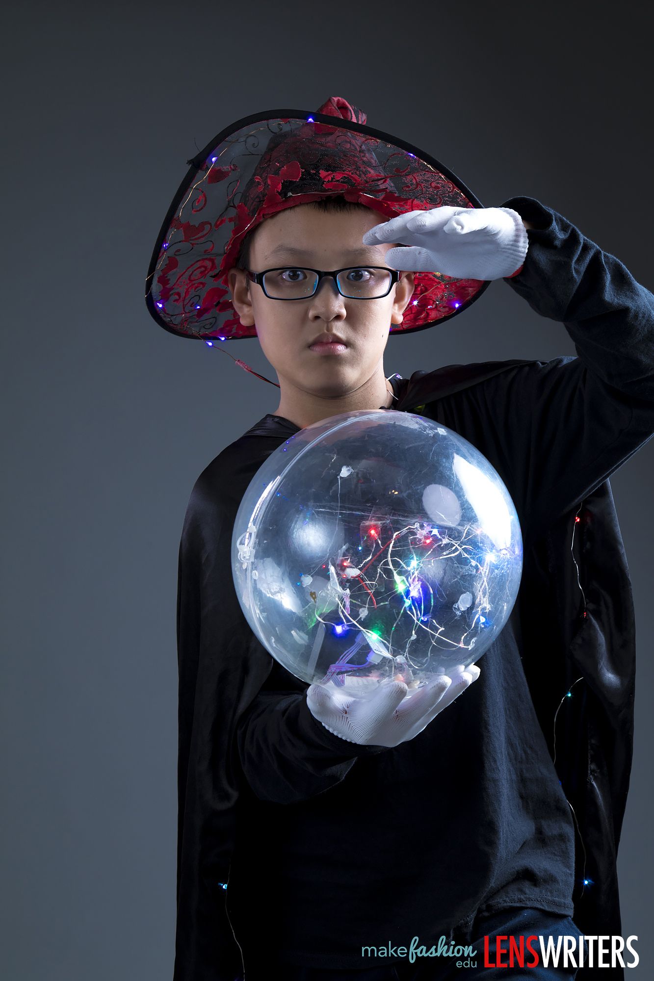 Student model holding transparent sphere with colorful LED circuit inside, wearing red embellished hat