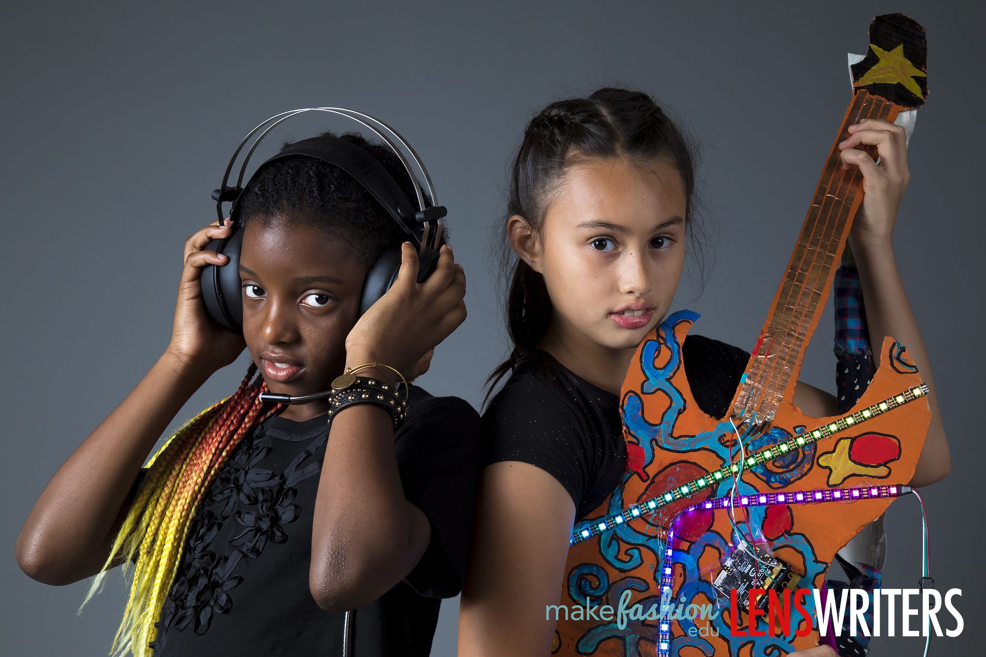 Student musician with LED-embellished orange guitar beside student with black headphones and yellow braided hair extensions