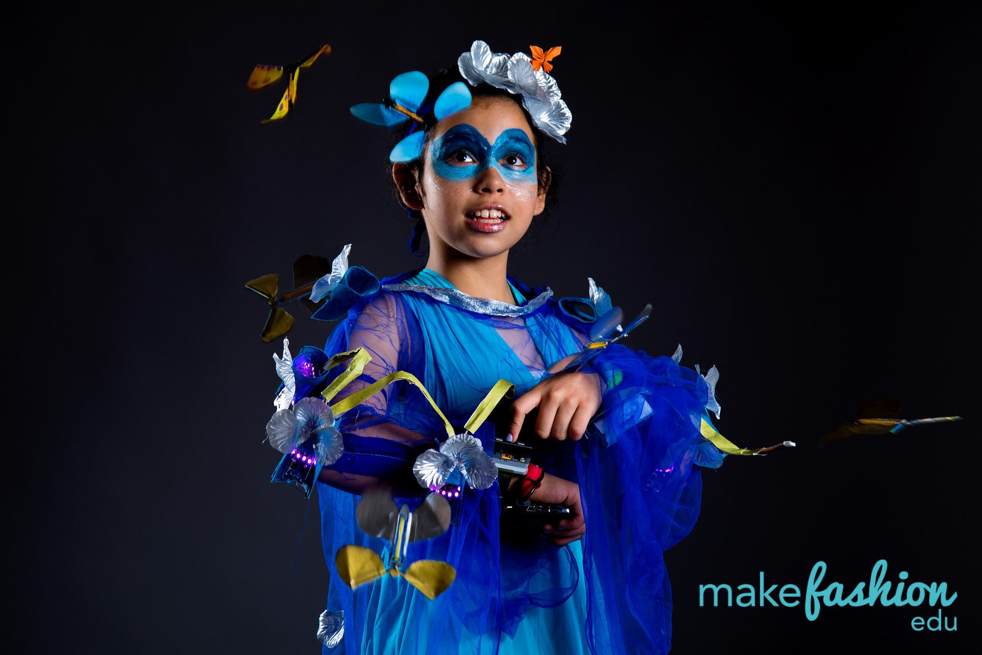 Student model in blue tulle dress with butterfly face makeup and LED-lit silver flower cuffs