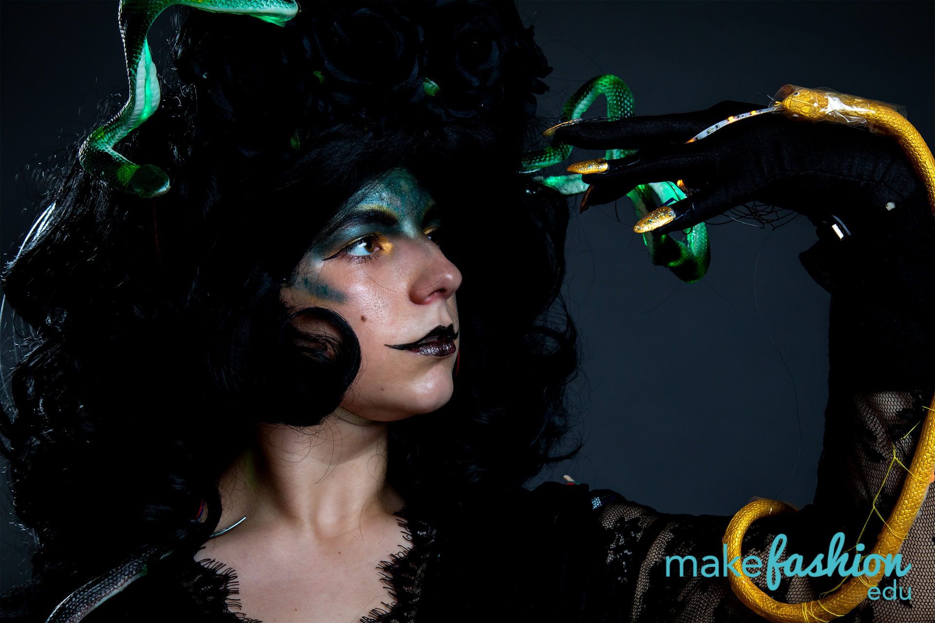Student model in theatrical makeup with green and gold snakes wound through hair and glove
