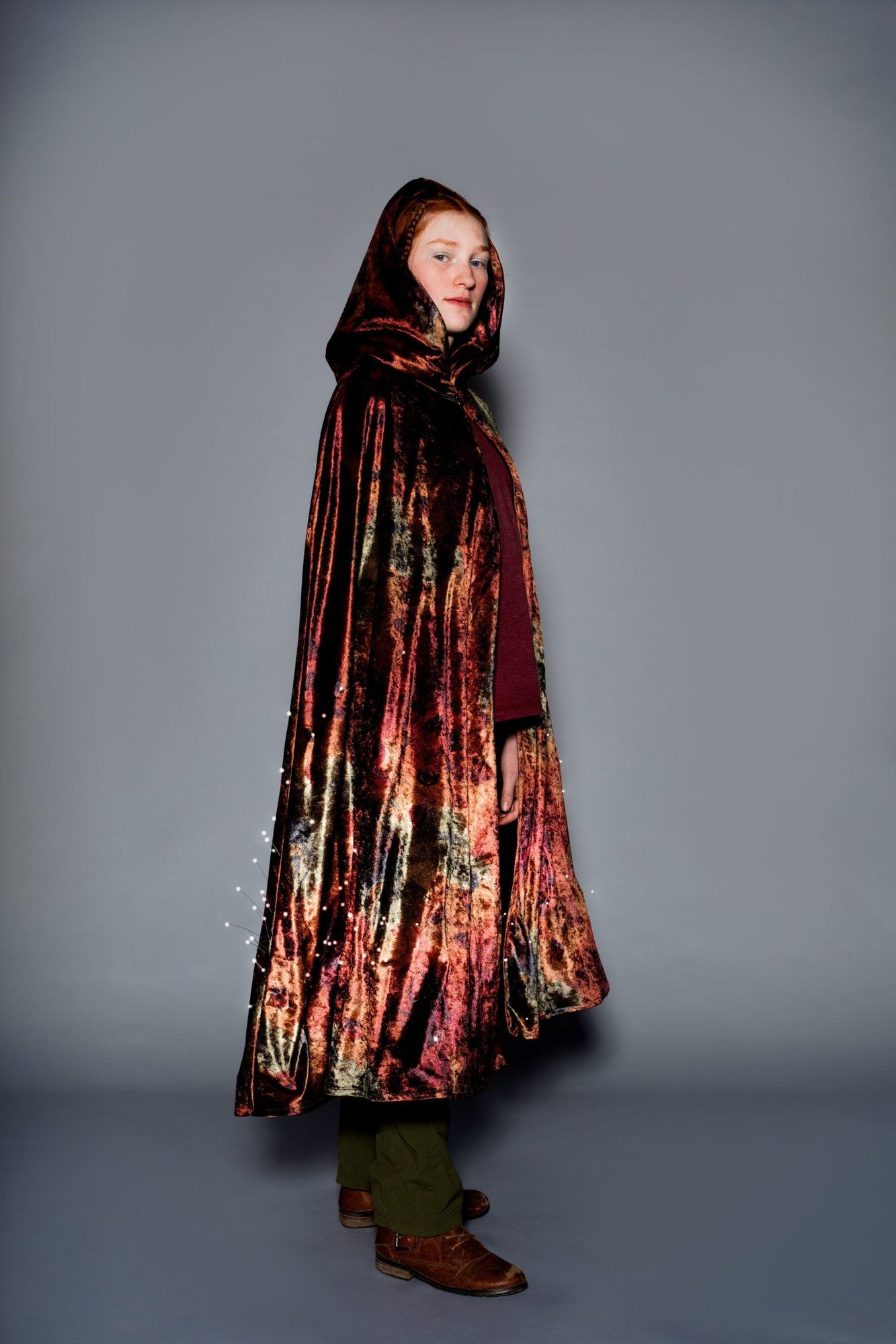 Student model in red and gold velvet hooded cape with LED accent lights along the hemline