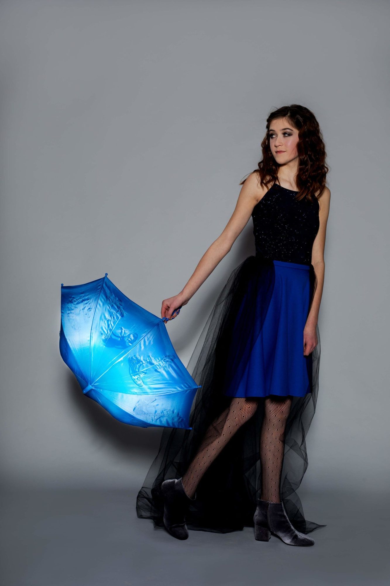 Student model holding glowing blue umbrella in black top, blue skirt, and black tulle train