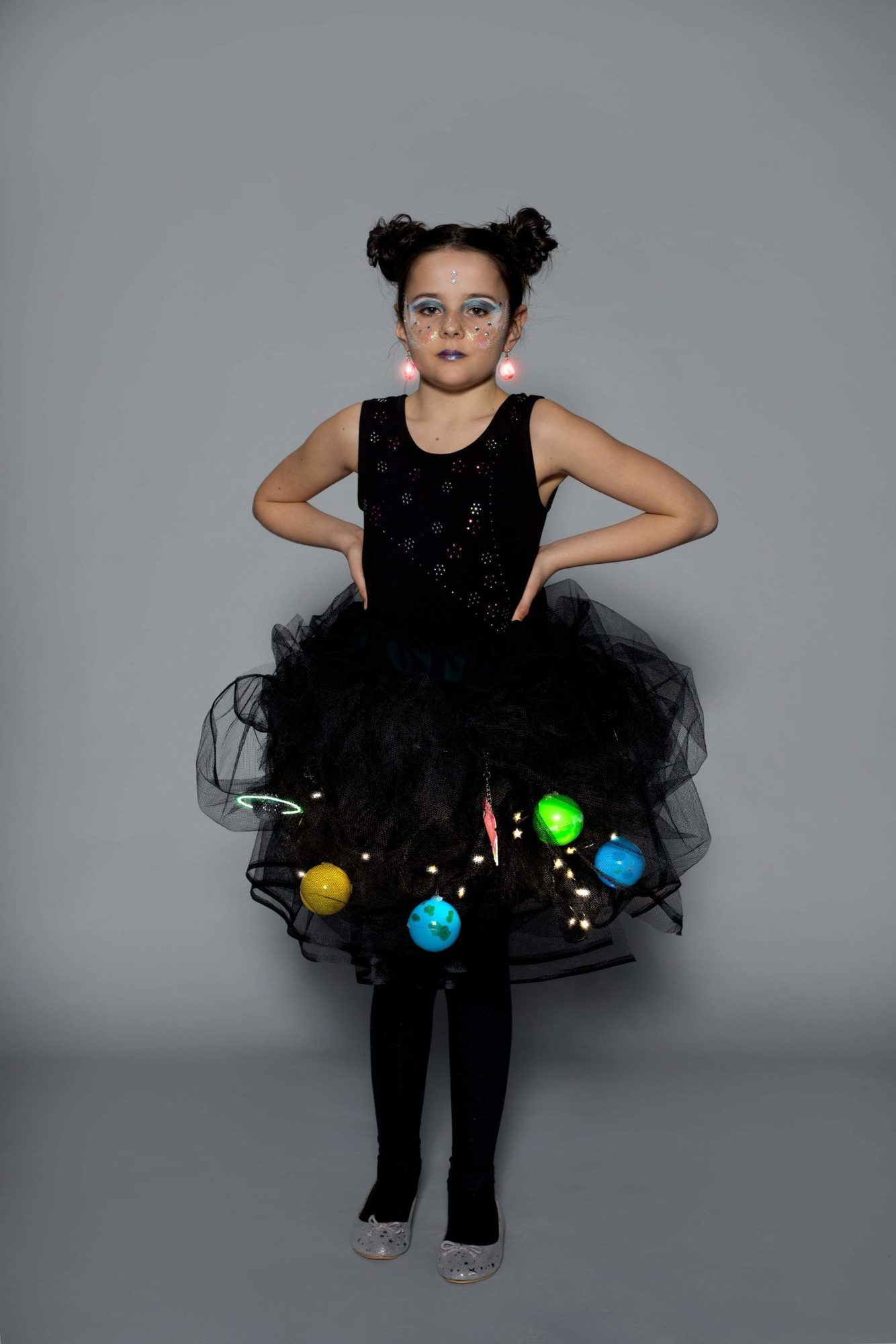 Student model wearing pink LED earrings with black tulle skirt displaying hanging colorful planet spheres