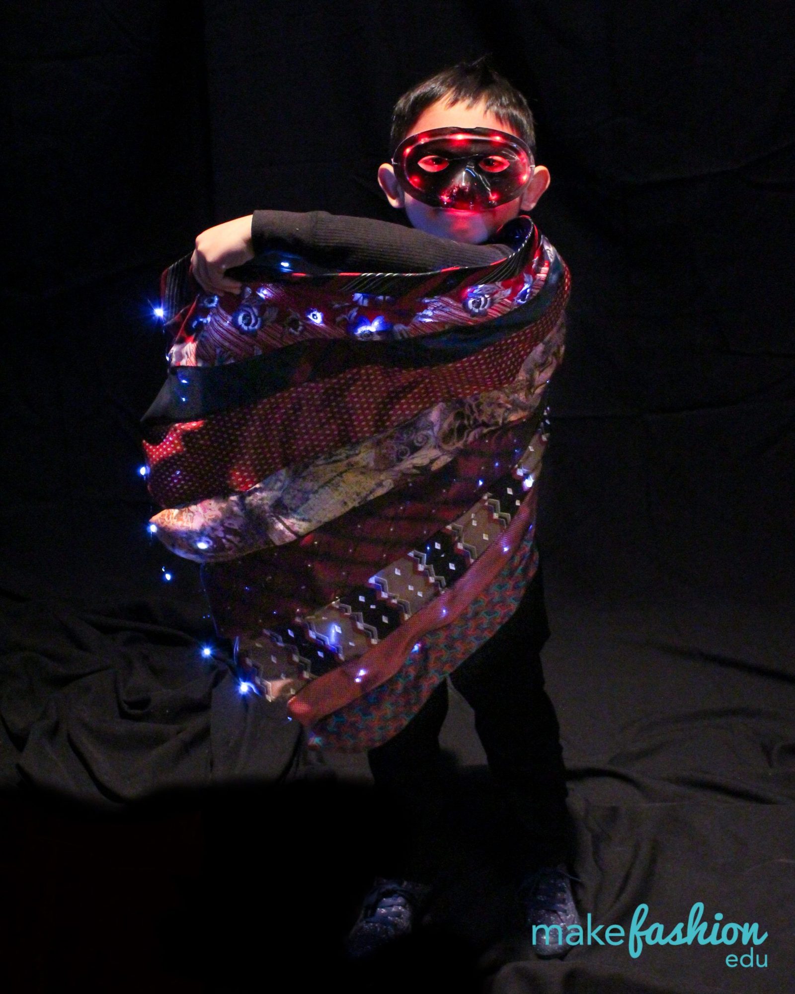 Student wrapped in patterned fabric with an illuminated red eye mask