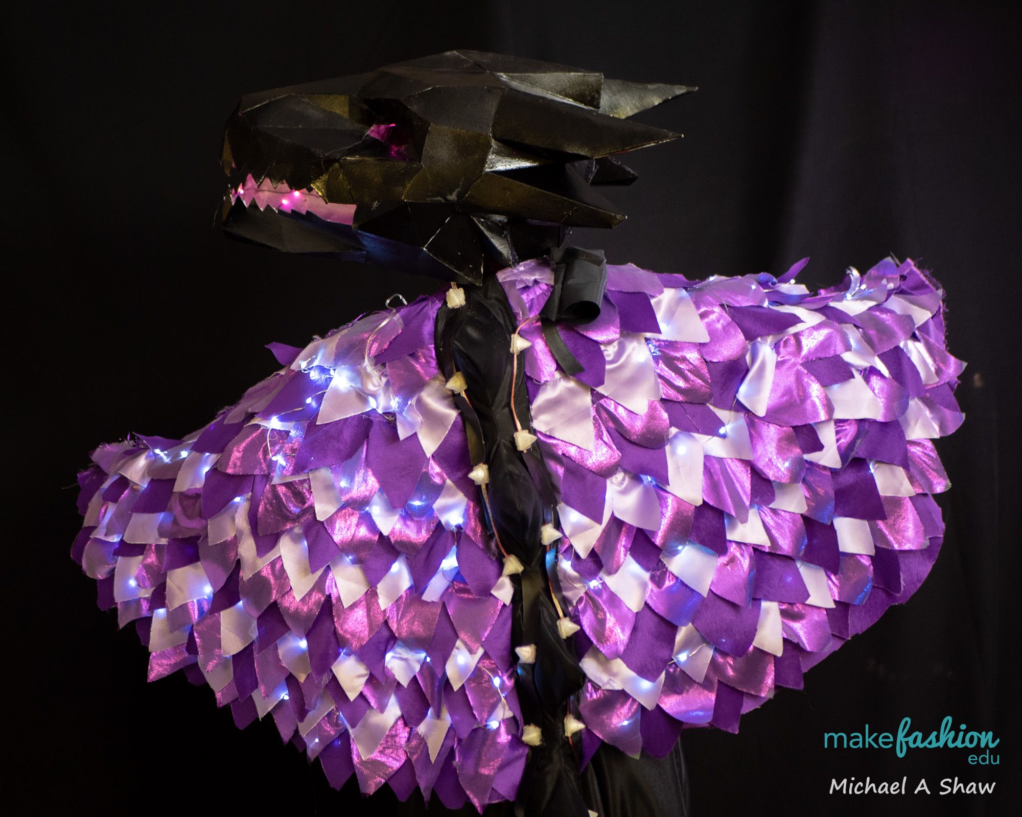 Dragon-headed cape with purple and white scale panels lit by fairy lights
