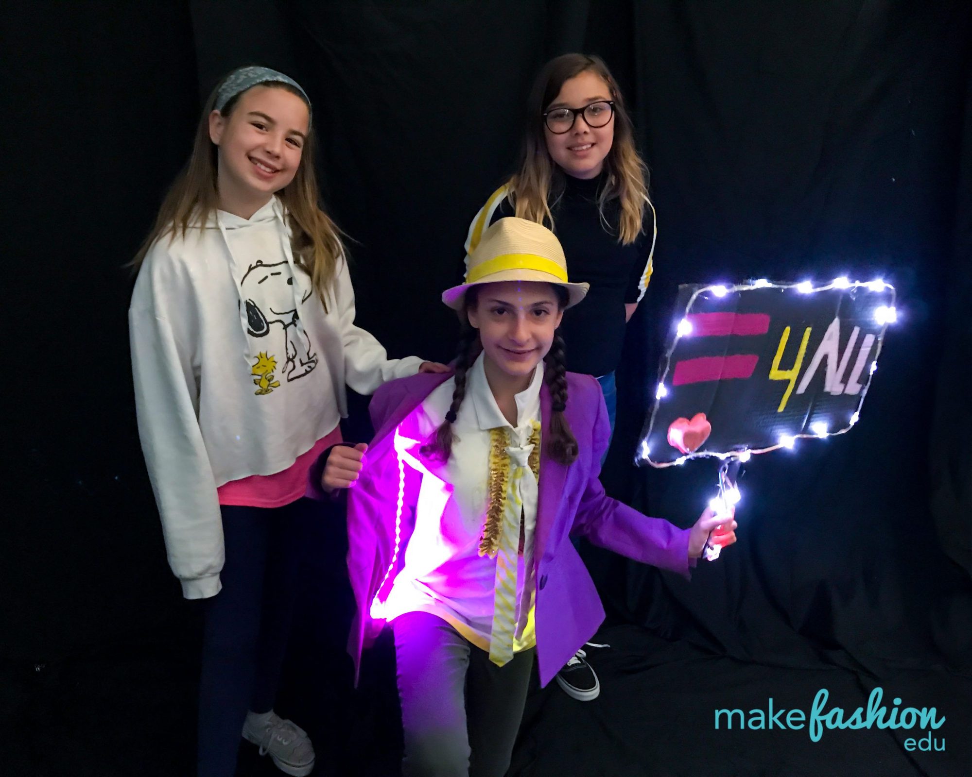 Three students with a light-up equality sign and glowing purple blazer