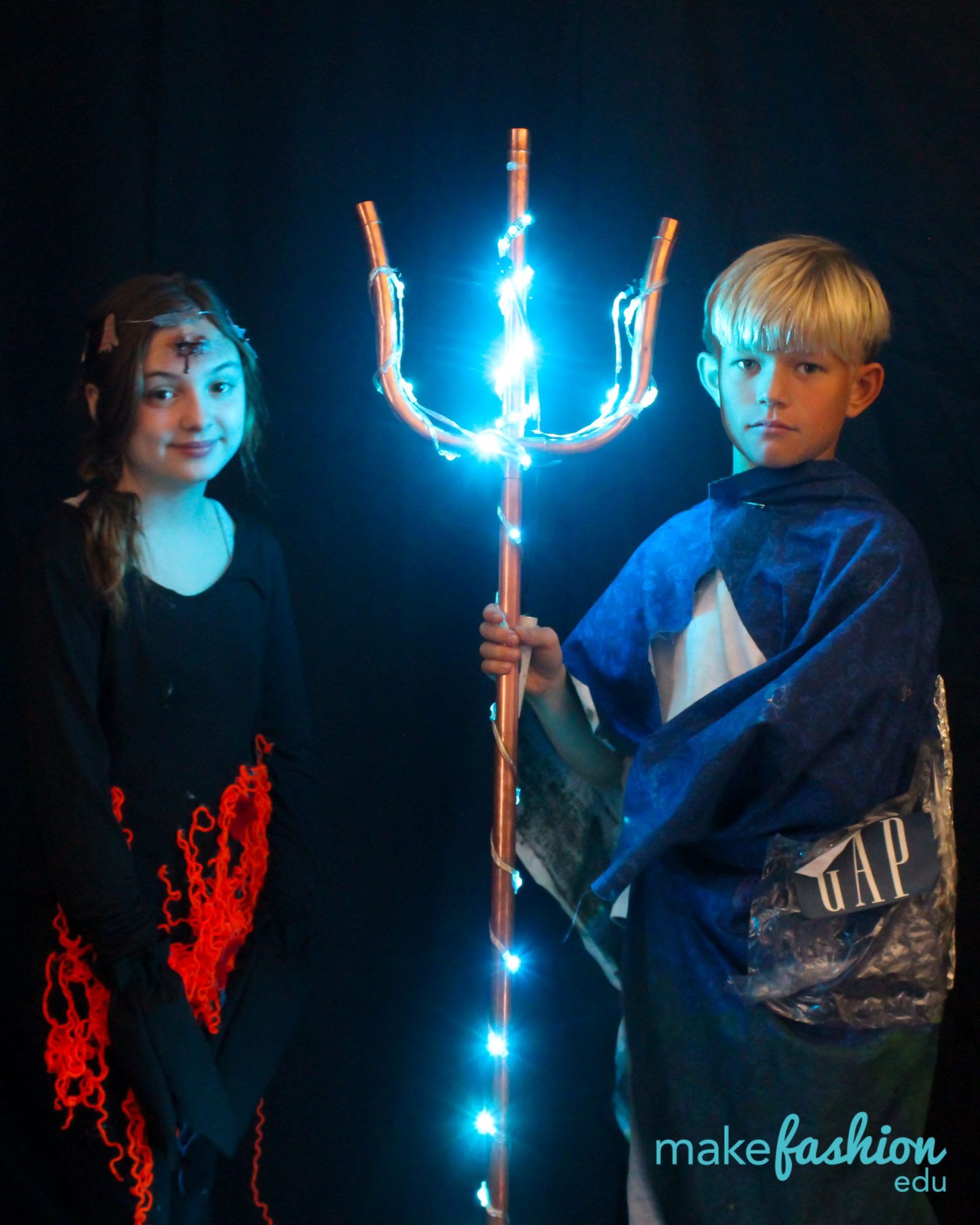 Two students with a glowing blue LED trident and red yarn-accented dress