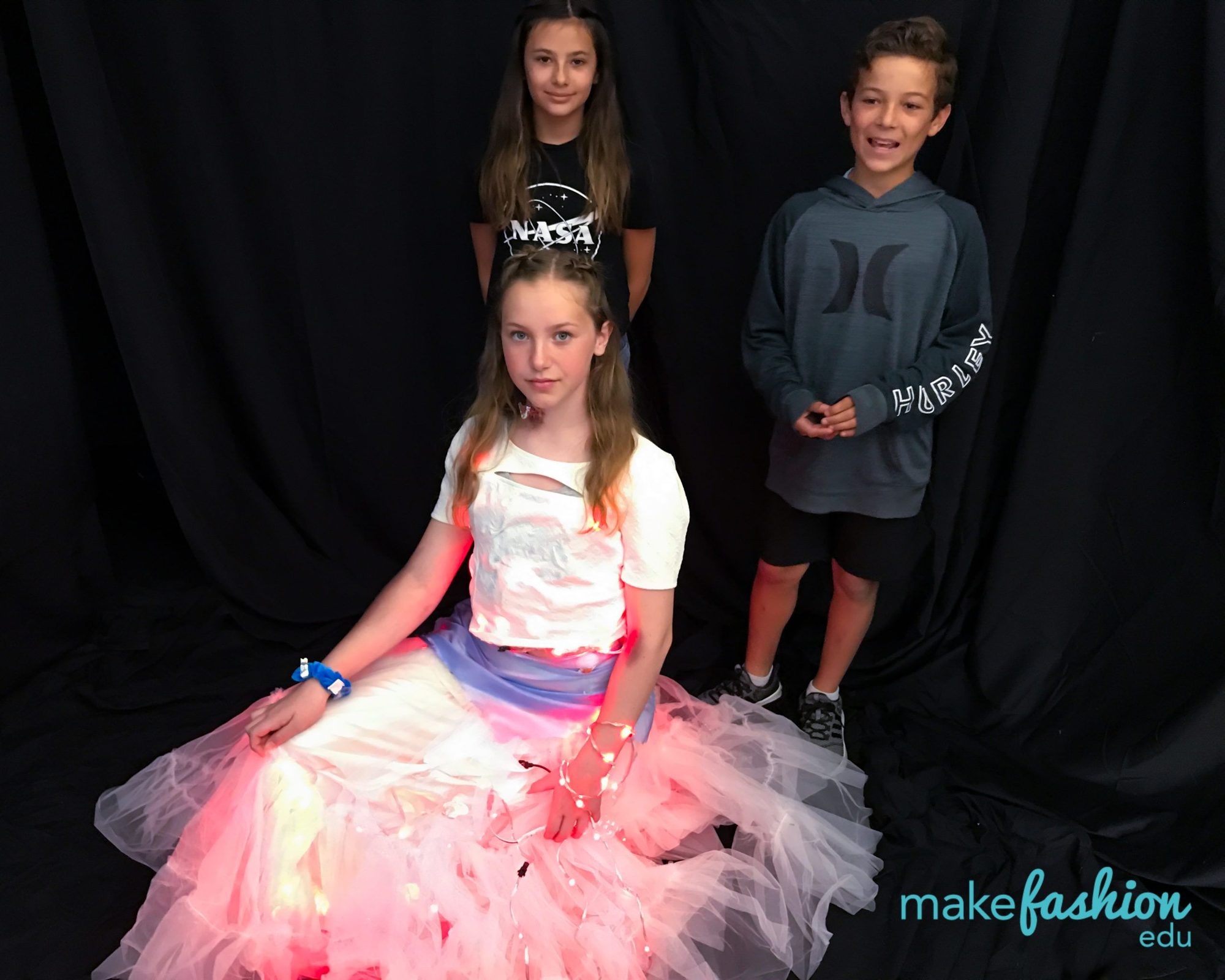 Student seated in a pink LED-lit tulle gown with two others standing