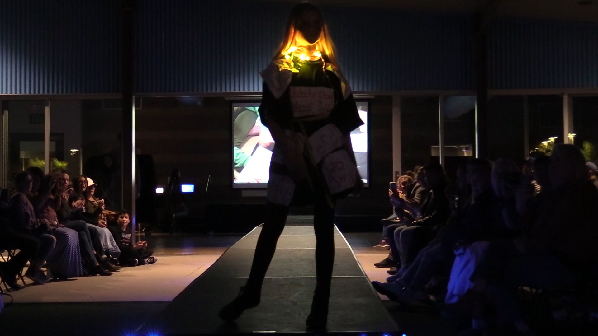 Student on runway from behind with paper tags on jacket and glowing amber collar