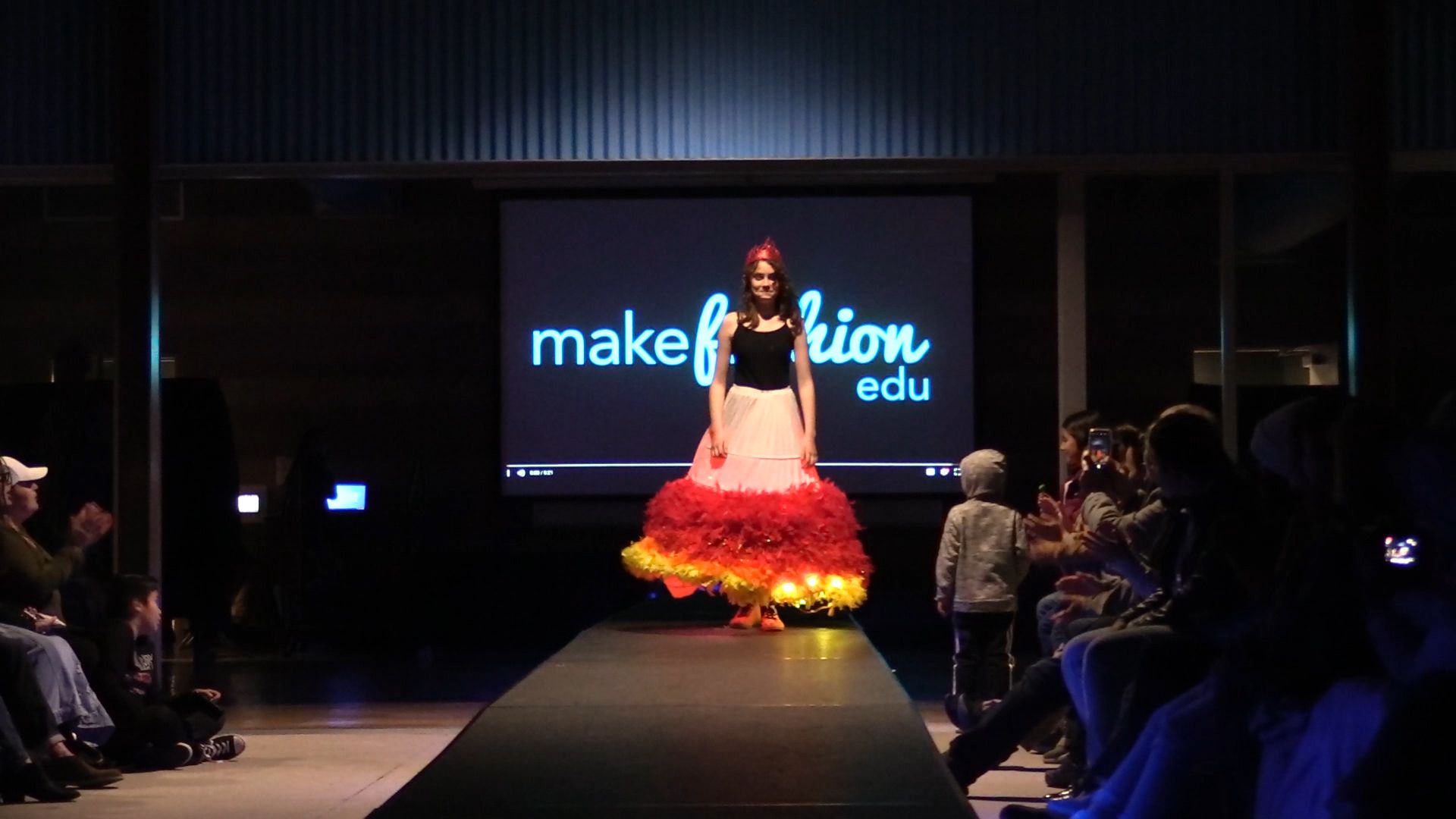 Student in dress with large red and gold LED-lit skirt on runway