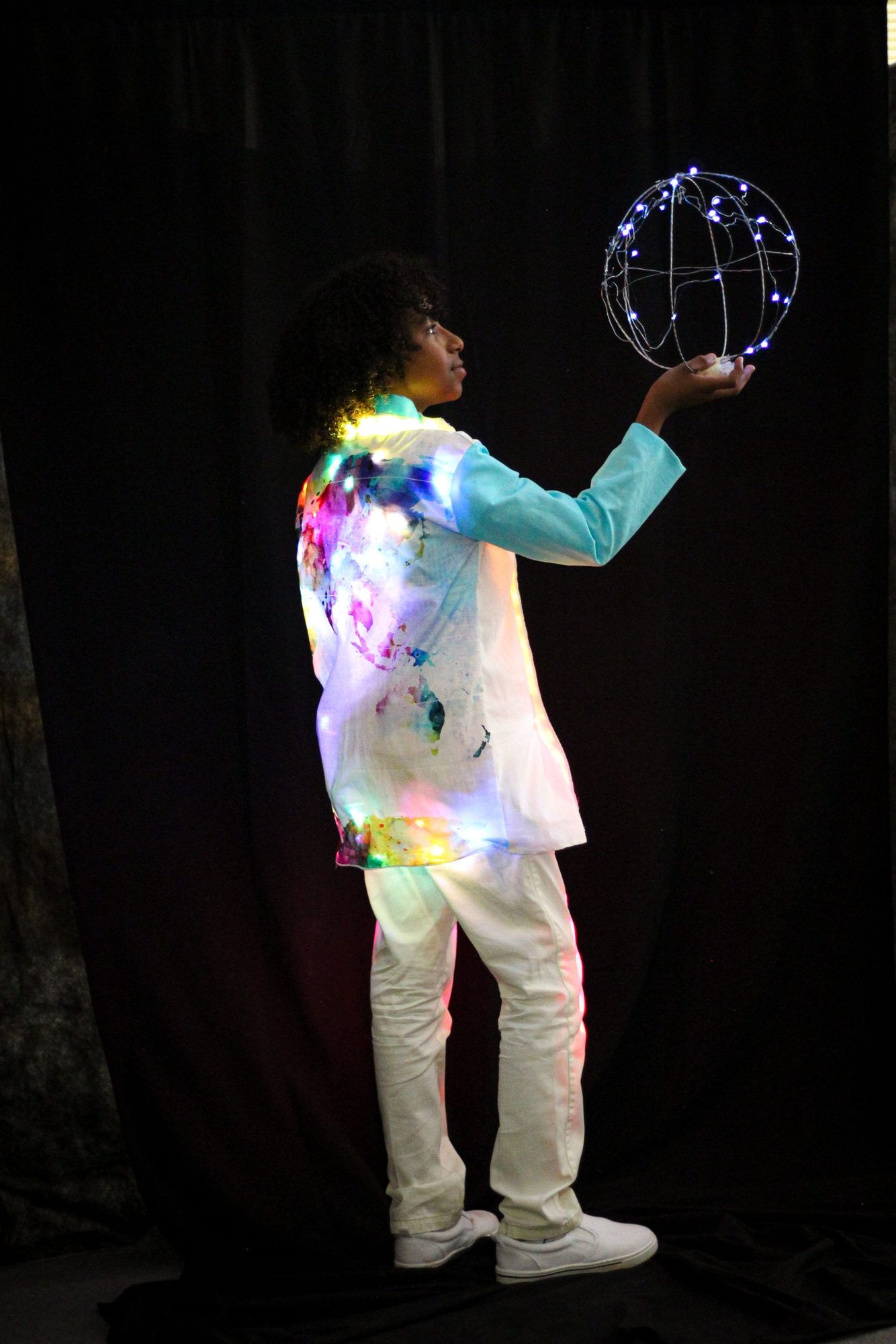 Student in white jacket with teal sleeves holding illuminated wire globe