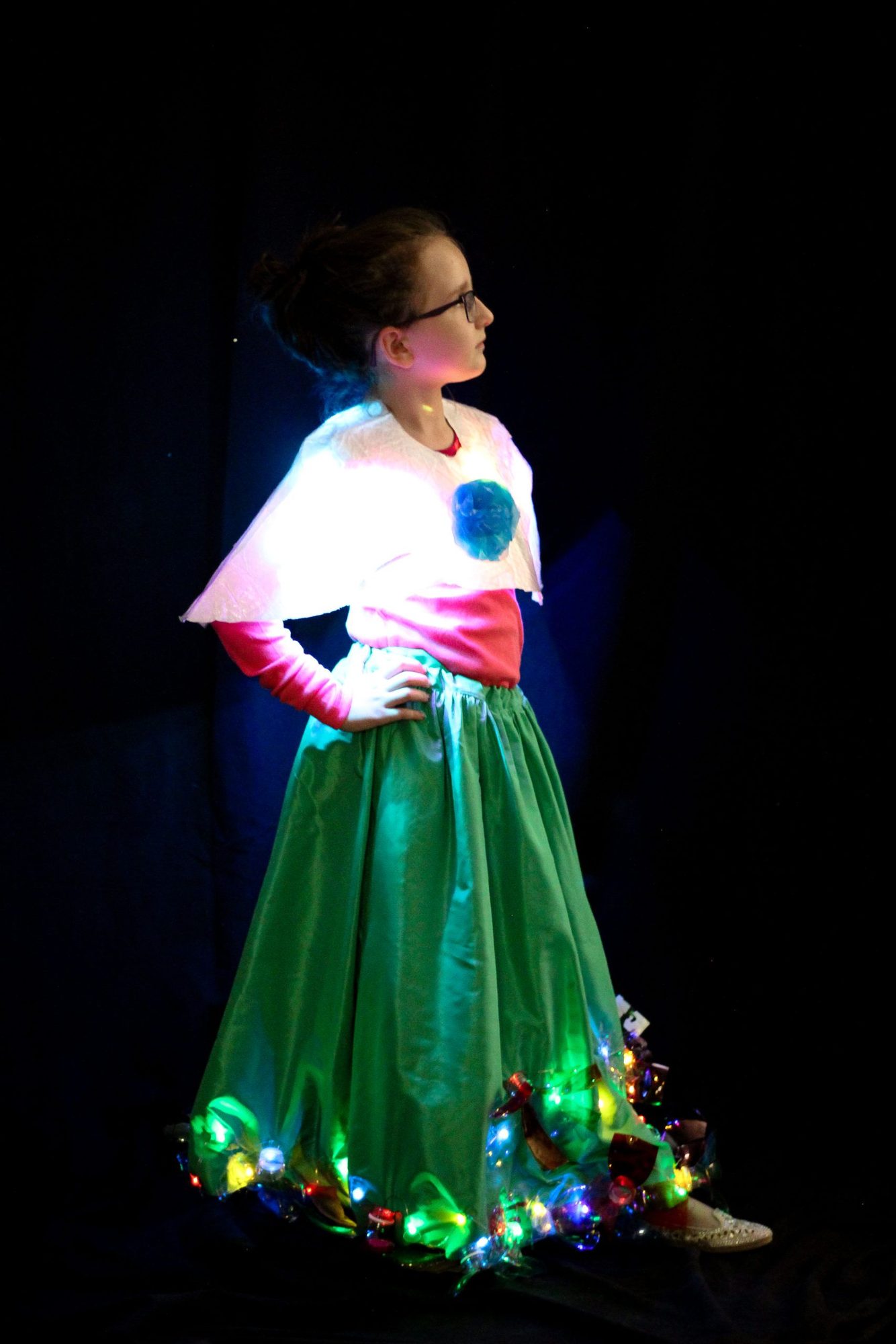 Student in dress with large green skirt decorated with glowing multicolor LED hem