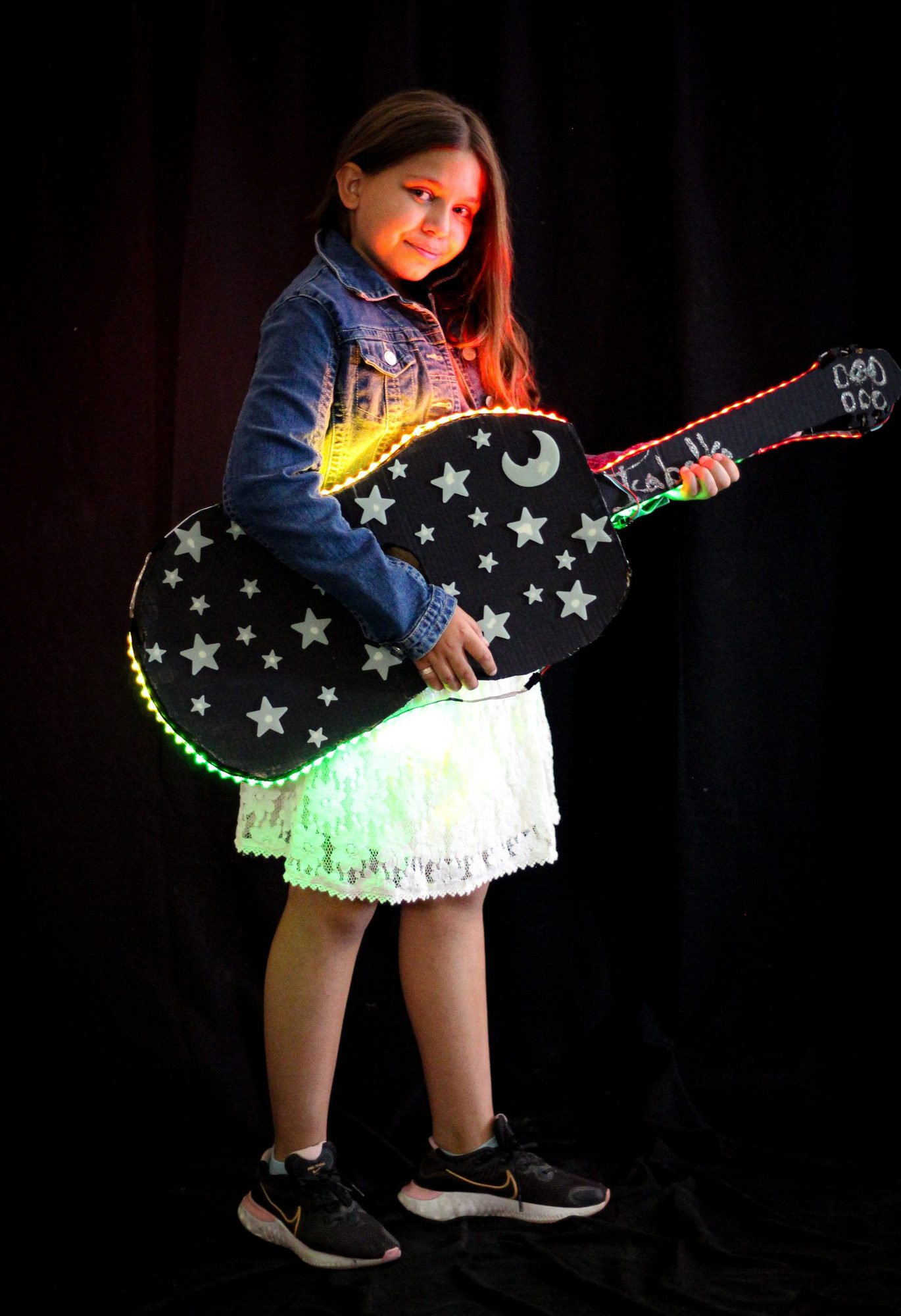 Student holding illuminated guitar with star and moon design and glowing edge lights