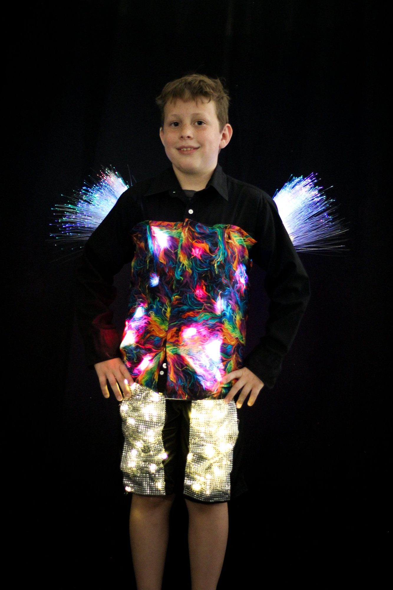Student in colorful light-up vest with sequined shorts and blue fiber-optic wings