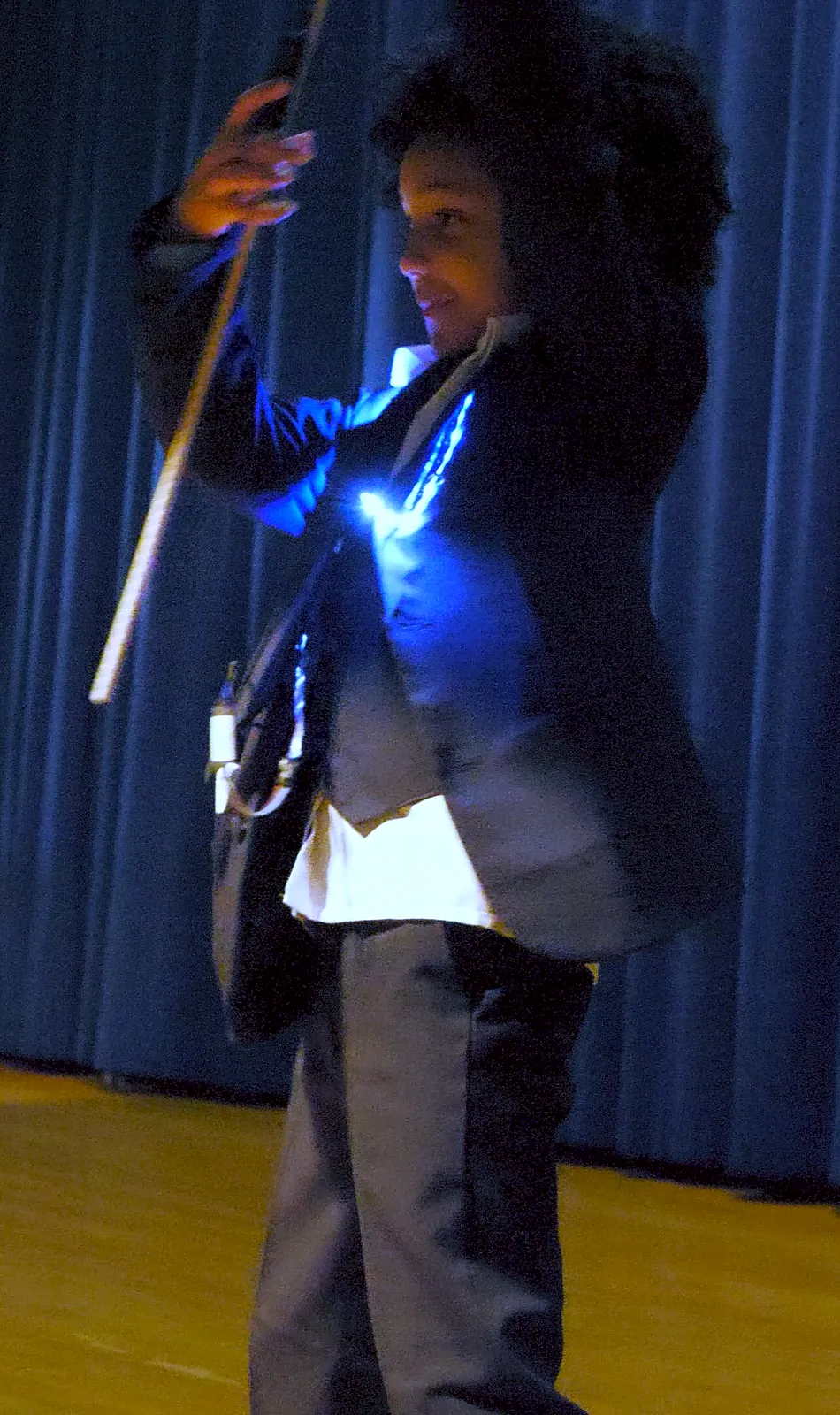 Student as Barack Obama in a dark suit lit with blue LEDs, standing on the auditorium stage