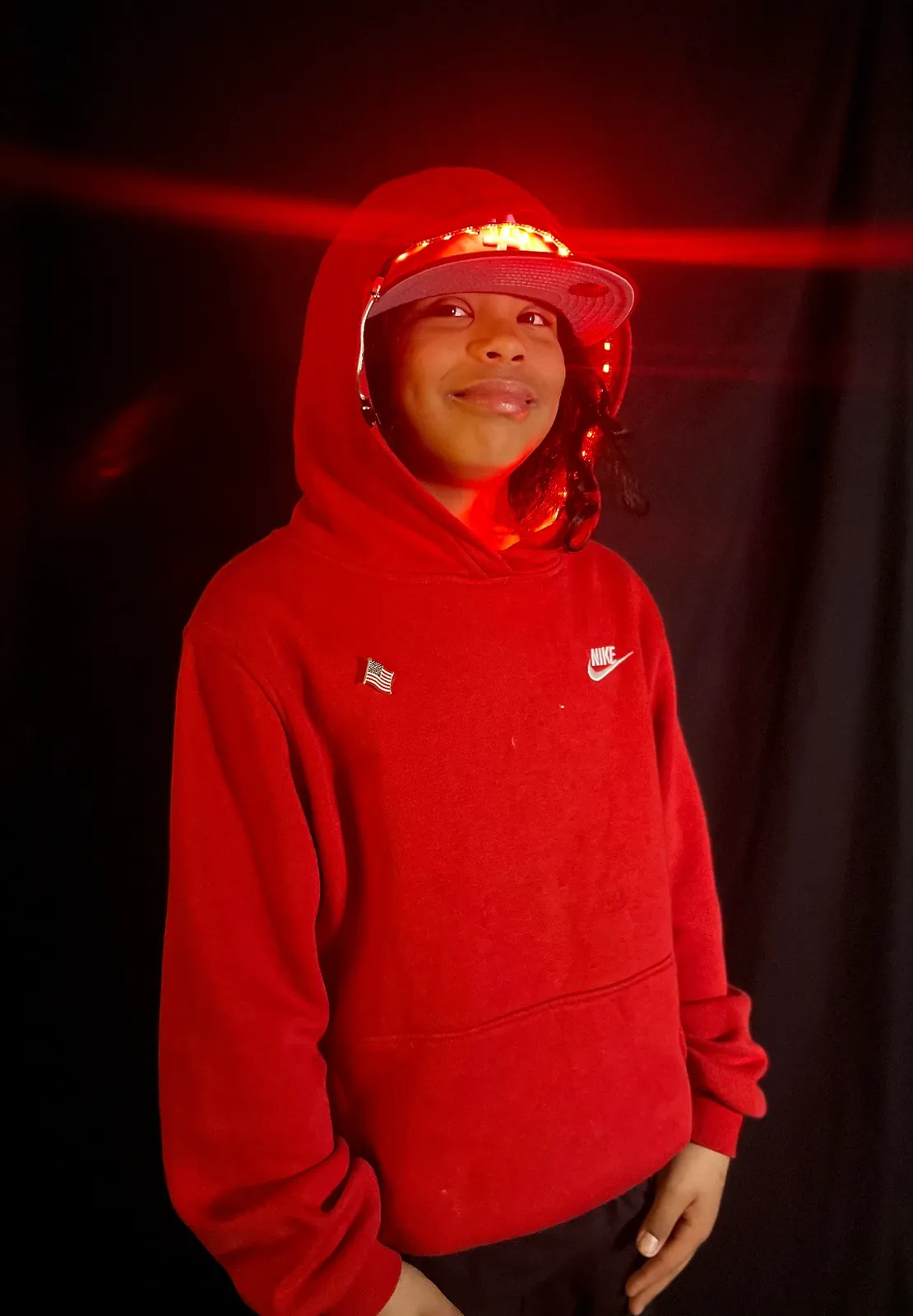 Student as Kendrick Lamar in a red hoodie with an American flag pin and a cap rimmed with glowing red LEDs