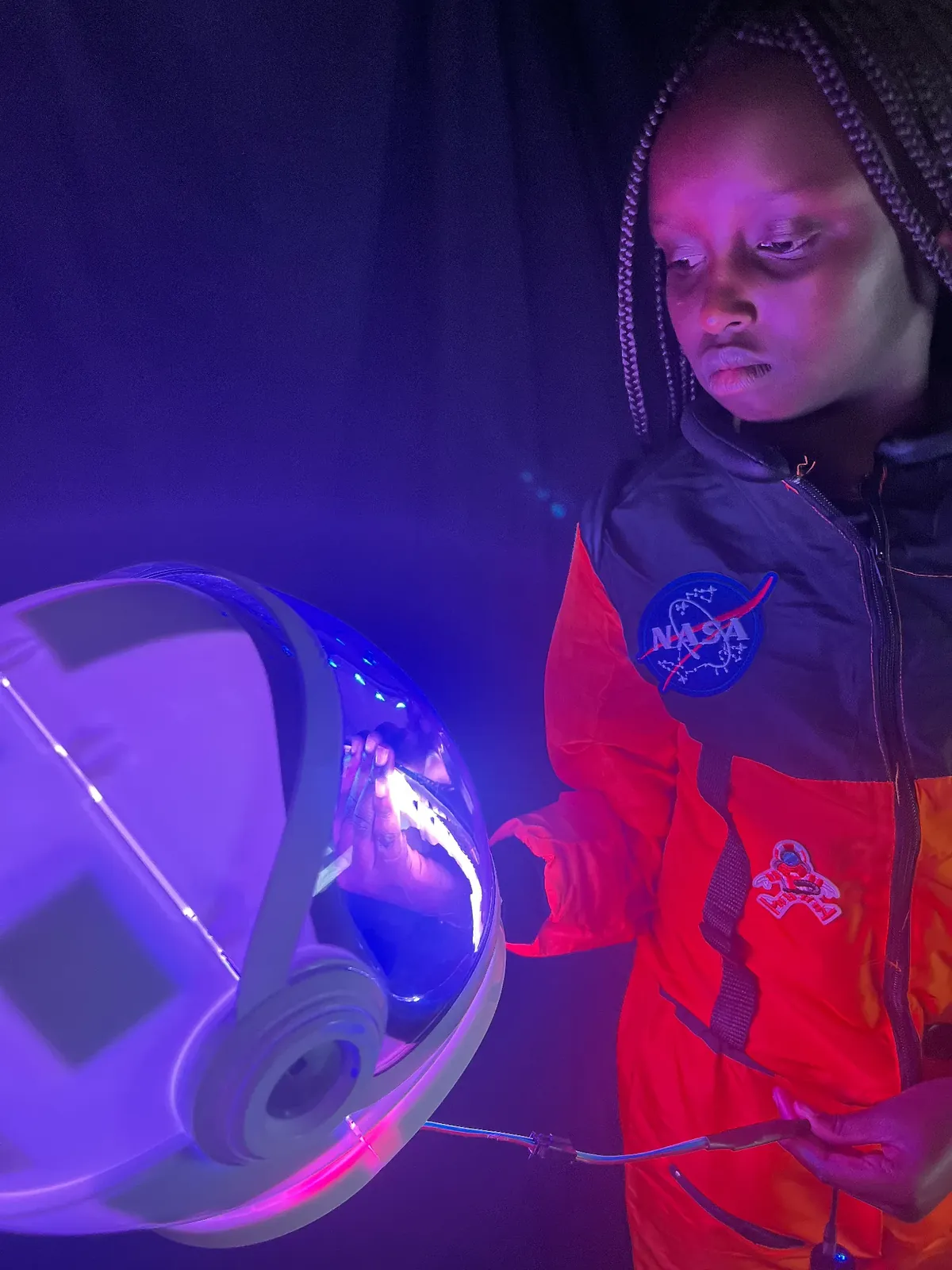Student as Mae Jemison in an orange NASA suit, holding her astronaut helmet and its LED wiring
