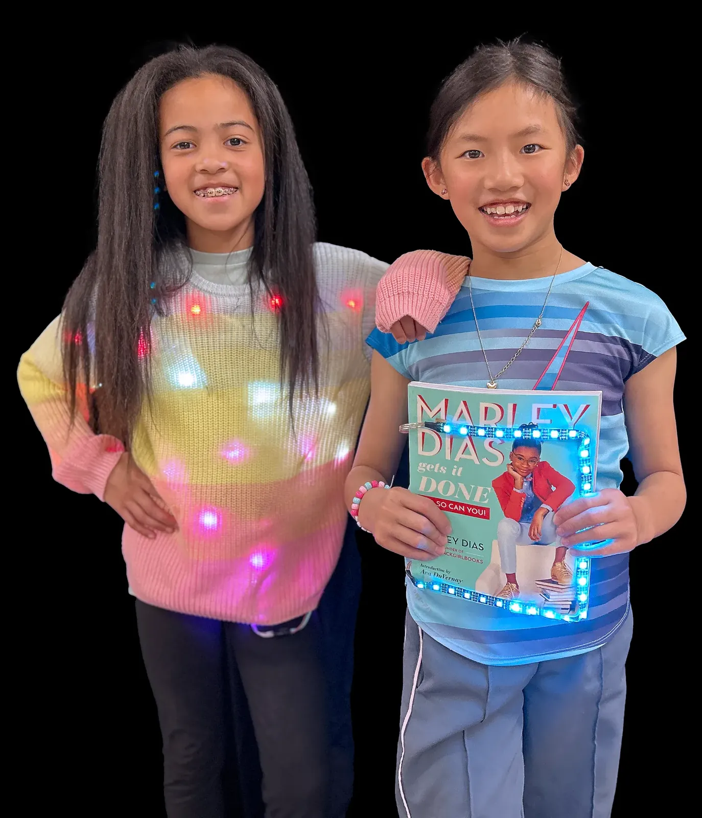 Two smiling students, one in a pastel sweater dotted with LEDs and one holding the book Marley Dias Gets It Done framed in blue LEDs