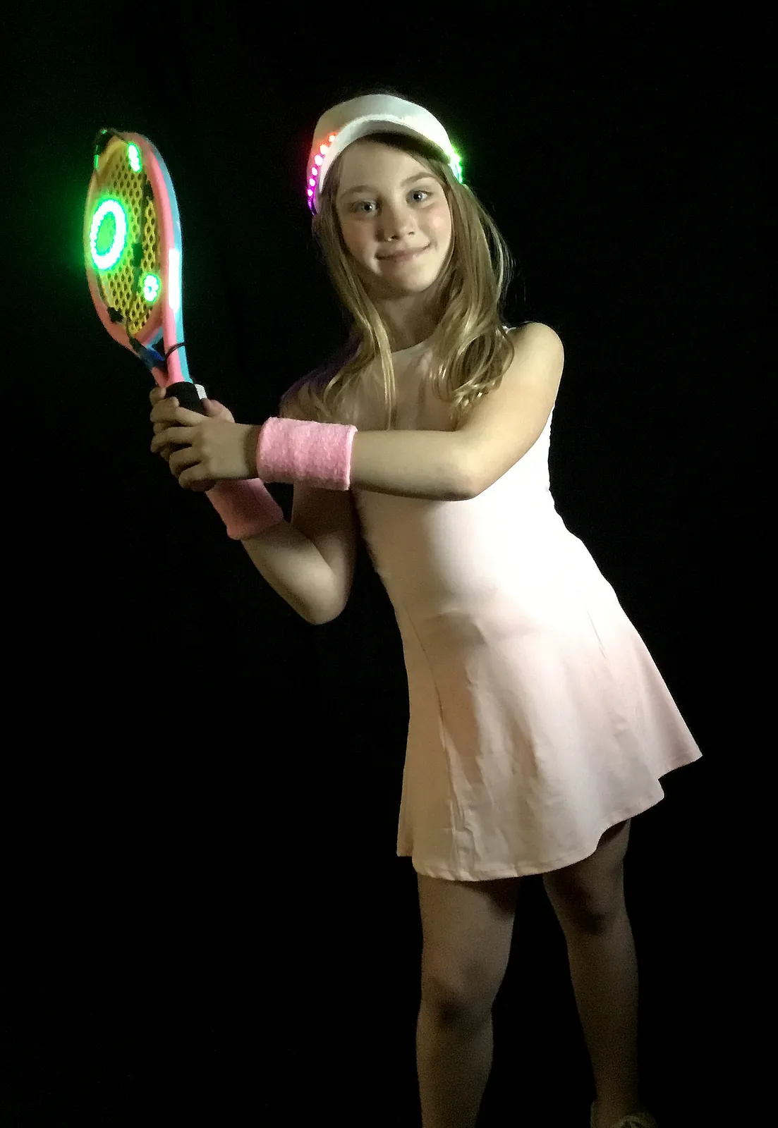 Student as Naomi Osaka in a white tennis dress, holding a racket and wearing a visor that glow with green LEDs
