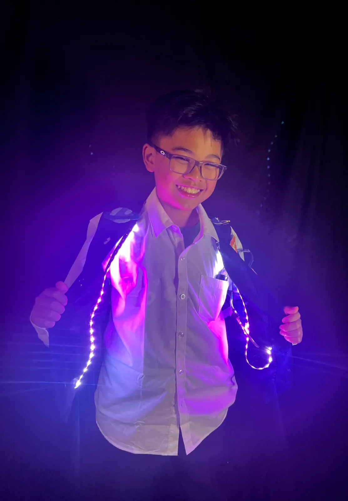 Student as Neil deGrasse Tyson holding open a dark vest lined with glowing pink LED strips