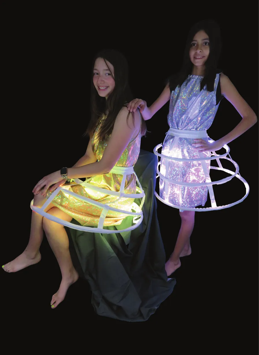 Celestial Neighbors: two students in metallic dresses over round skirt cages, one glowing gold as the sun and one silver as the moon