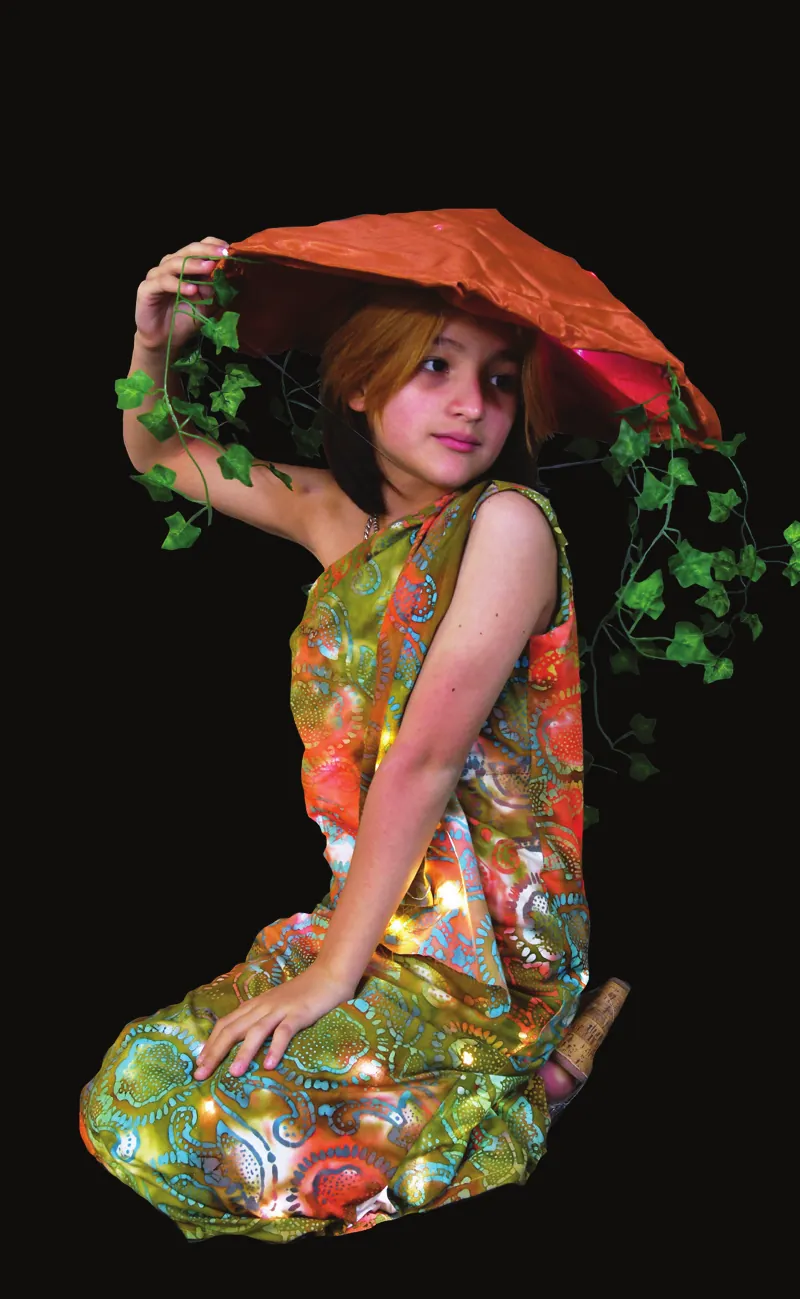 Fungi Fashion: student kneeling in a patterned dress, wearing a large red mushroom-cap hat trailing green vines