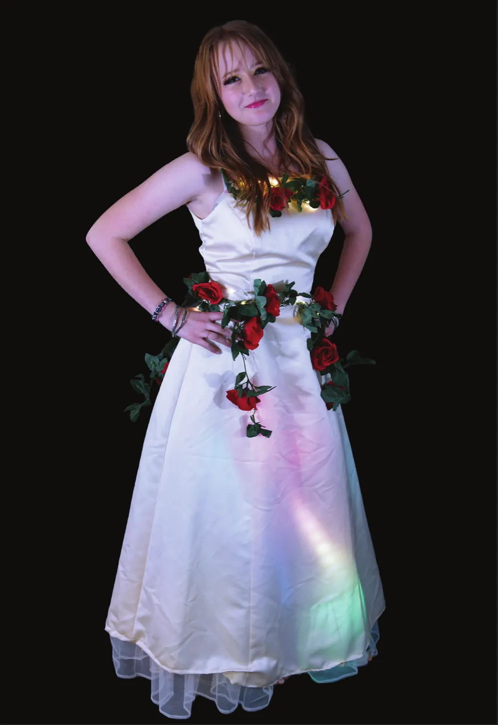 La Quinceañera: student in a white gown trimmed with red roses and green leaves, lights glowing in the skirt
